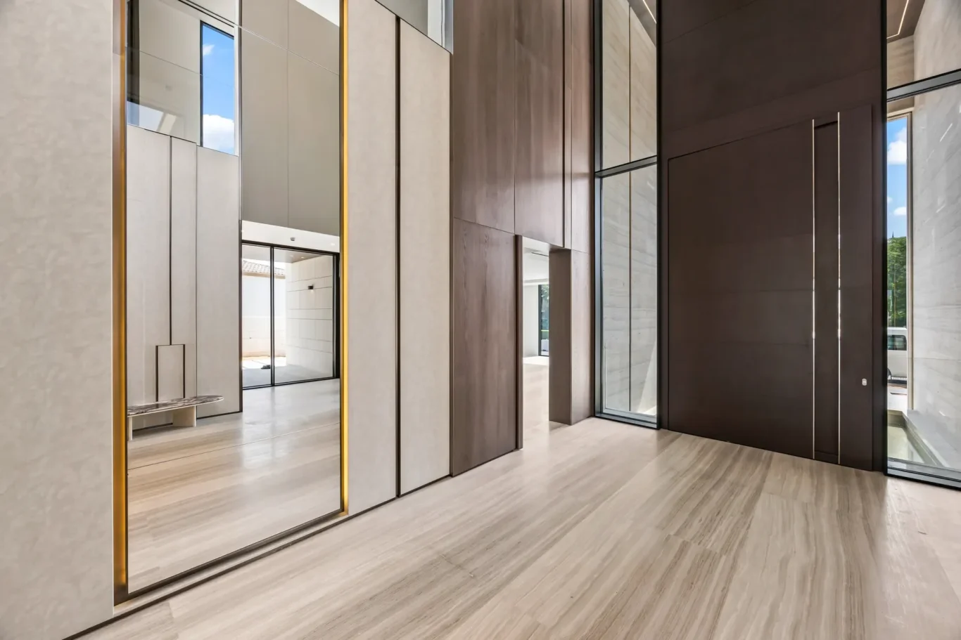 Modern lobby interior with tall beige marble panels, glass doors, and mirrors along a light wood floor.