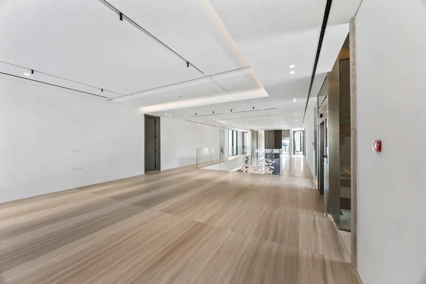 Bright modern office hallway with light wood flooring, white walls, and a glass railing down the center corridor