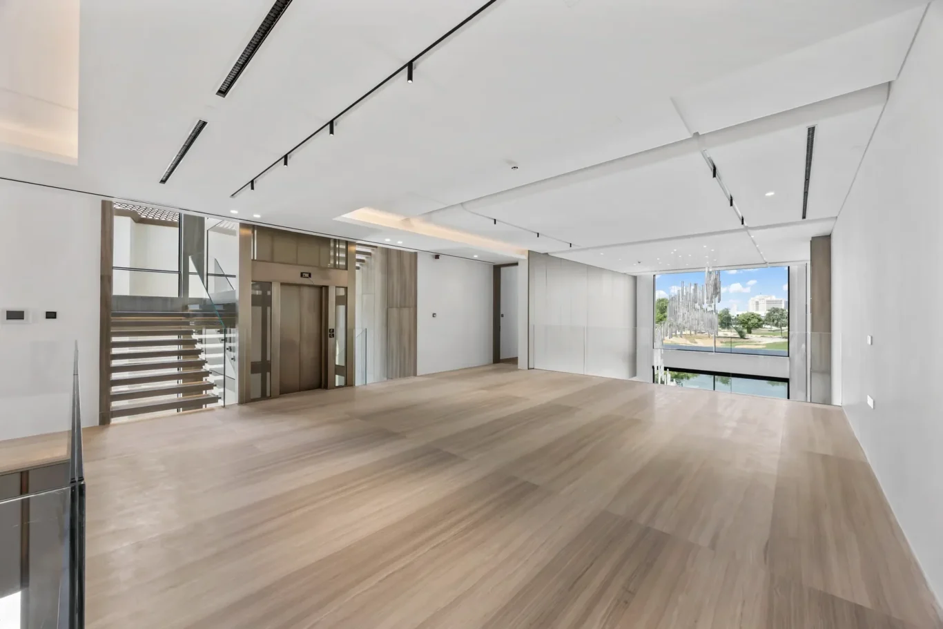Modern open lobby with wood floors, glass railing staircase, and an elevator by the wall, large window overlook outside.