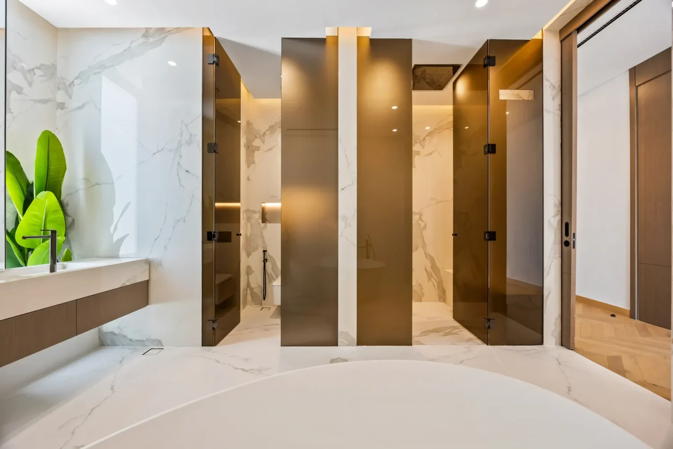 Contemporary bathroom with marble walls, bronze glass shower partitions, and a green plant by the sink area.