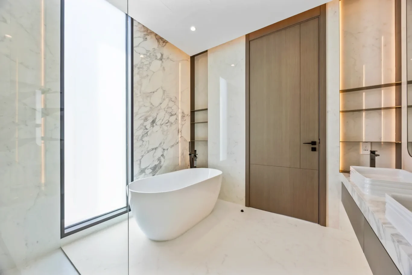 Luxurious marble bathroom with a freestanding oval tub, glass shower, and wooden cabinetry.