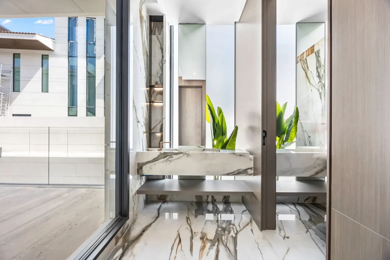 Modern marble bathroom with a floating vanity, veined marble surfaces, and green plants near large glass doors