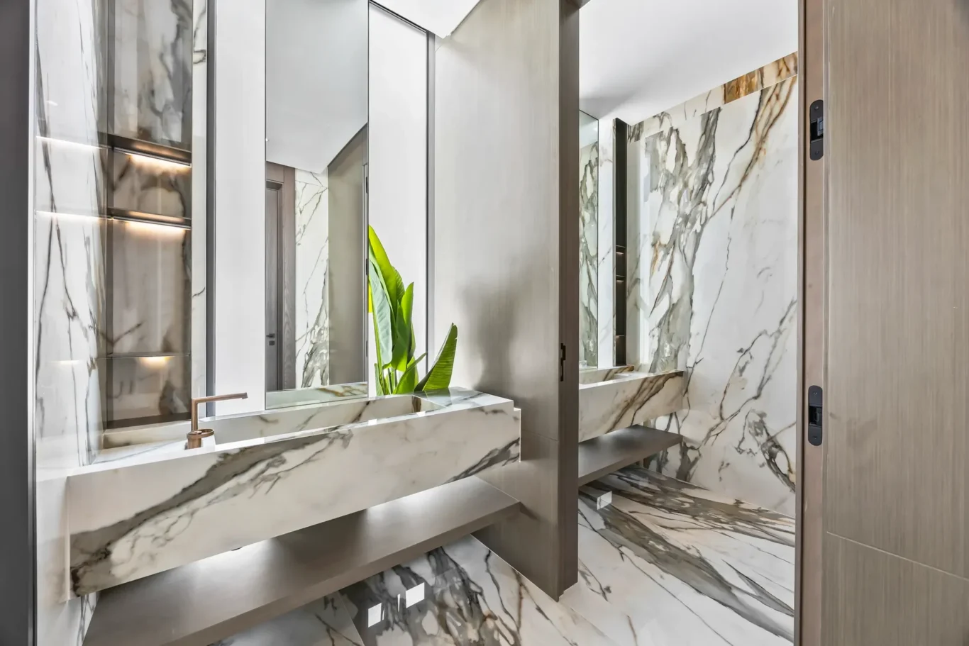 Luxurious marble bathroom with a long marble countertop, single bronze faucet, and tall mirrored walls reflecting marble surfaces.
