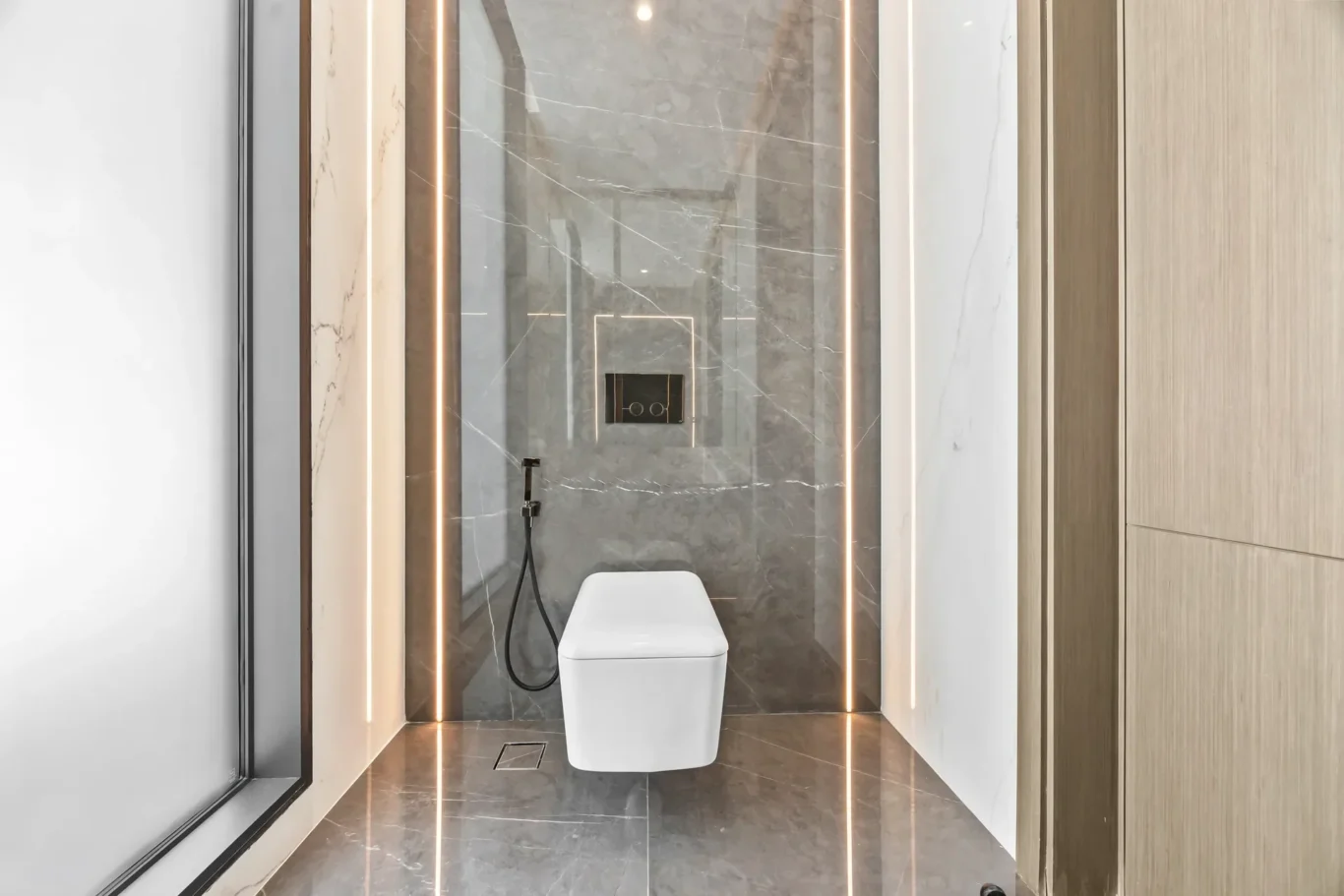 Modern marble bathroom with a sleek wall-mounted toilet and vertical LED light strips along marble walls, viewed through a glass door.