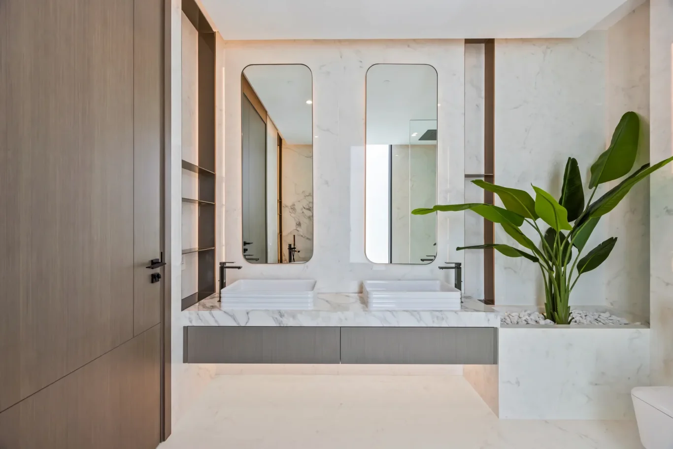 Modern bathroom with a marble countertop, two rectangular sinks, and tall rounded mirrors.