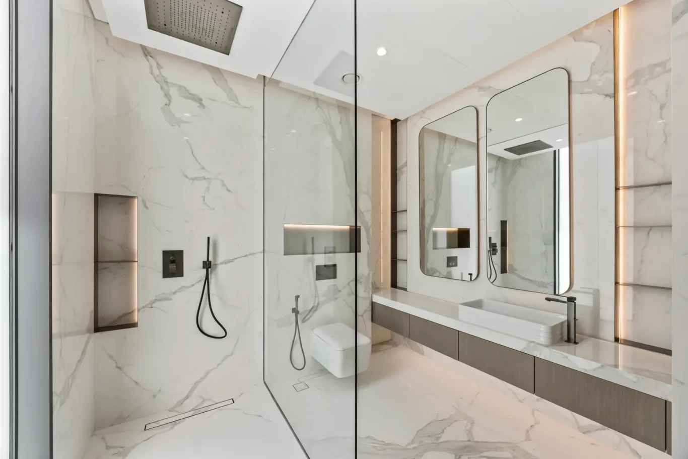 Luxurious marble bathroom with glass shower enclosure, double vanity, and large rounded mirrors.