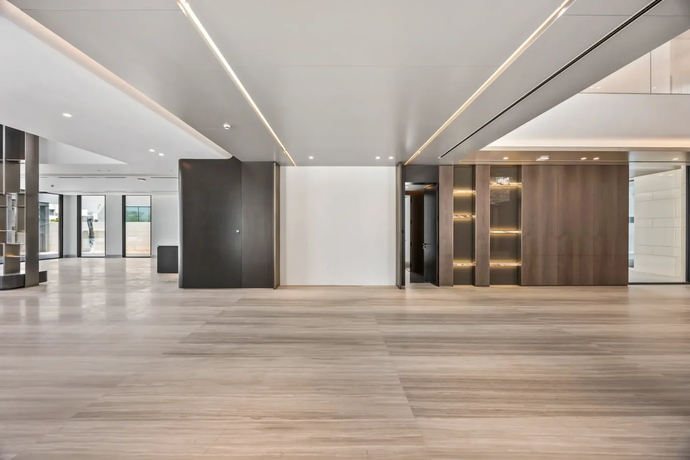 Spacious modern office lobby with wood floors, gray columns, and glass entry doors at the far end.