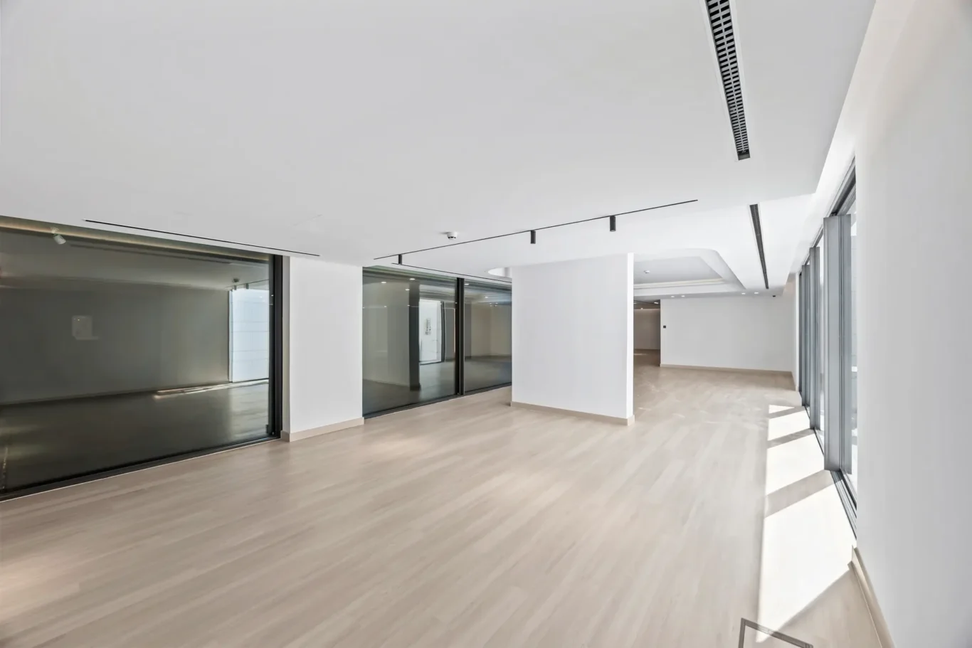 Empty modern office space with white walls, large glass partitions, and light wood flooring. (Informative)