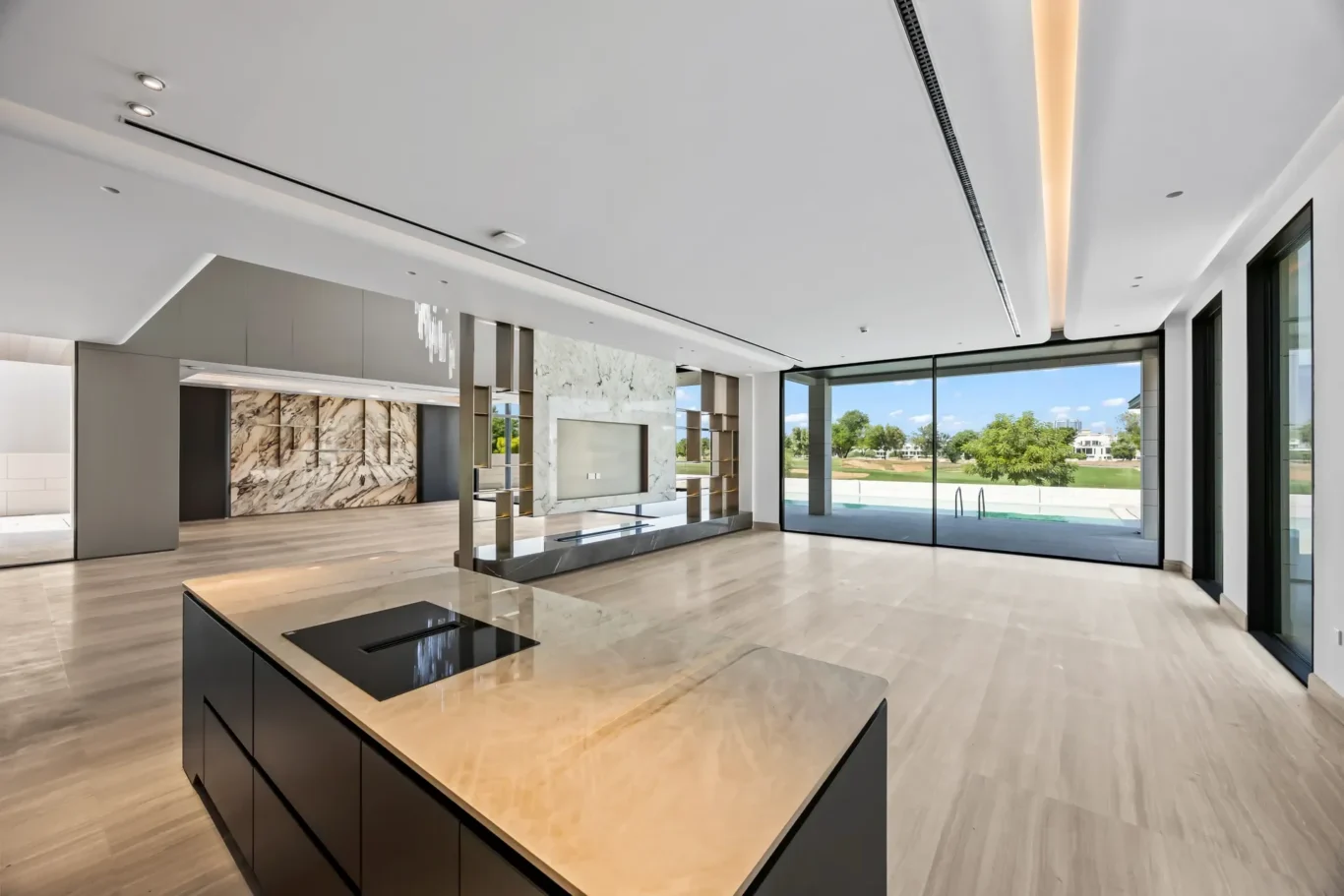 Open-concept kitchen with a marble-topped island, dark base cabinets, and large glass doors opening to a sunny backyard.