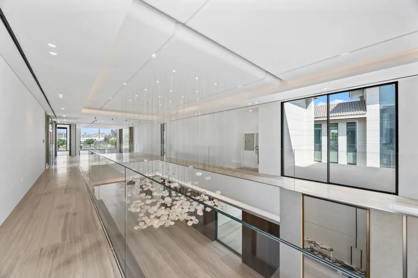 Bright modern hallway with glass balustrade and a hanging glass ball chandelier, large windows reveal an exterior building.