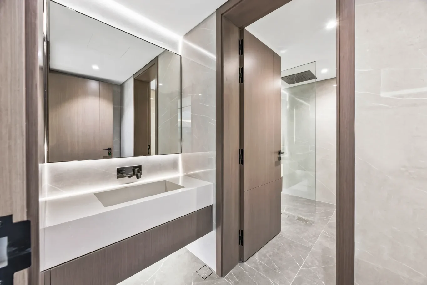 Modern bathroom with large rectangular sink, marble walls, and wood cabinetry reflected in a wide mirror.