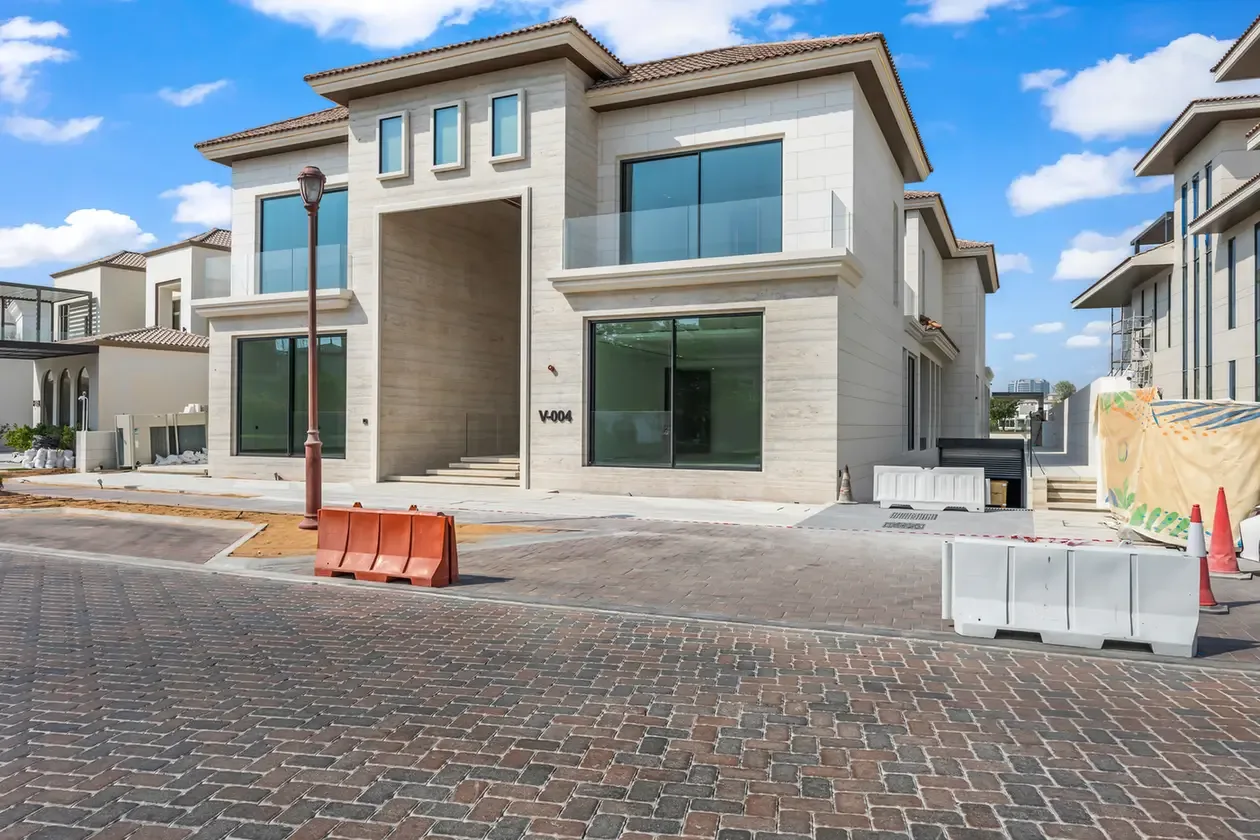 Front view of a modern two-story house under construction with large glass windows and a covered entrance, set along a cobblestone street with construction barriers nearby.