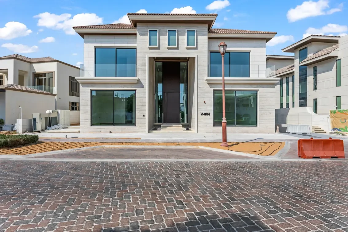 New modern two-story house under construction with large glass windows and a central entryway, facing a brick-paved street.