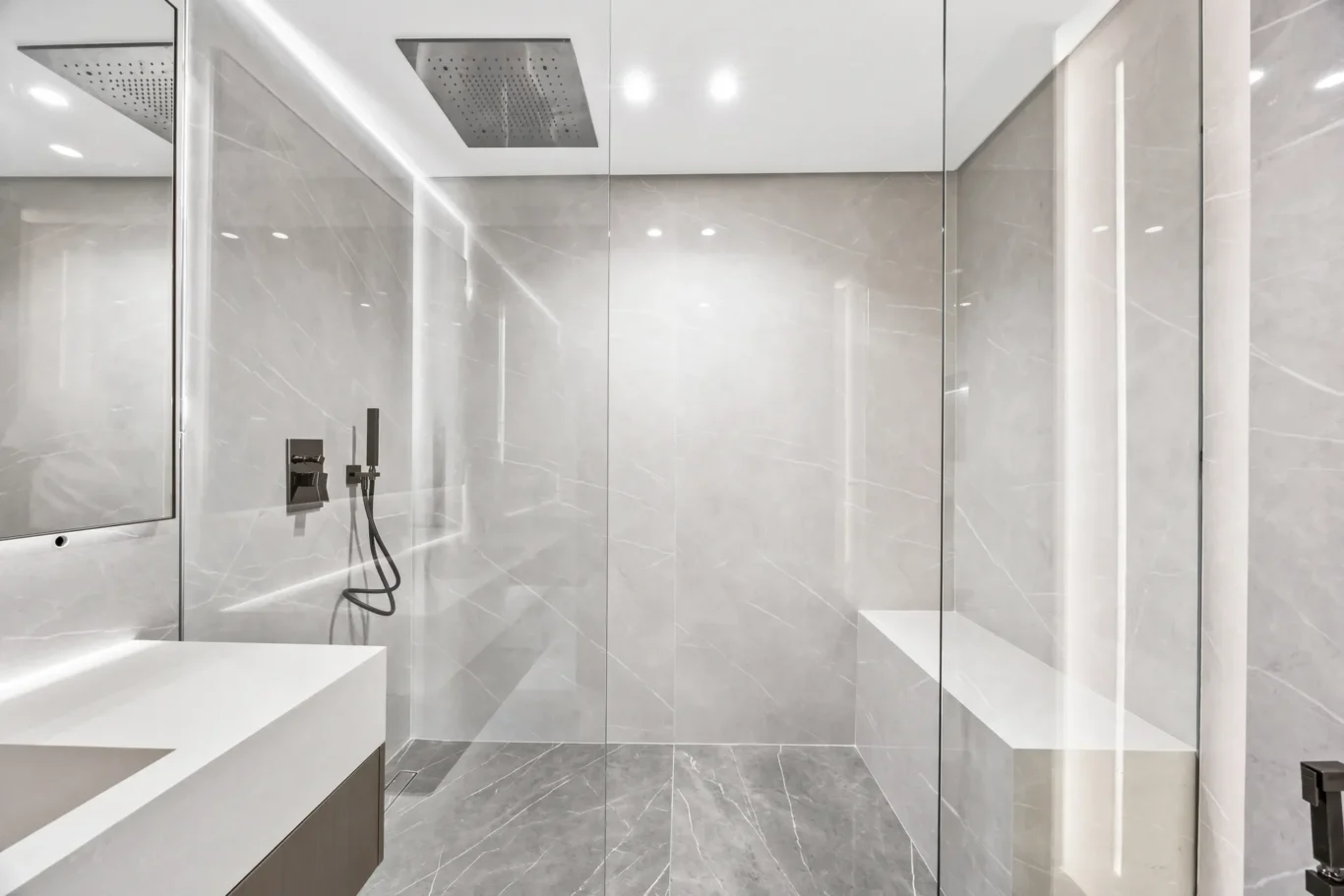 Modern marble bathroom with a glass shower enclosure, rainfall showerhead, and wall-mounted controls.