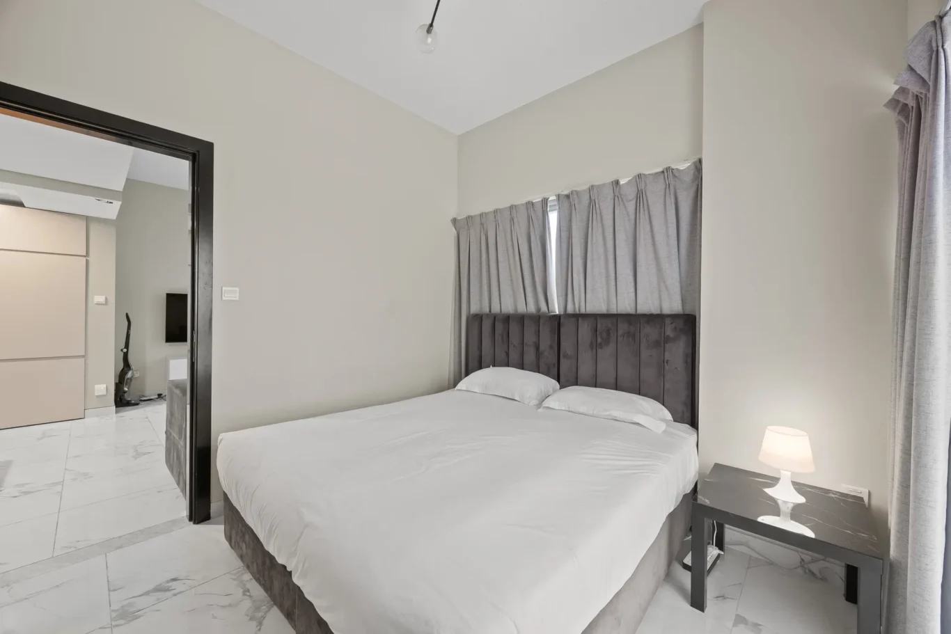 Modern hotel bedroom with white bedding, a gray upholstered headboard, and marble-tile floor