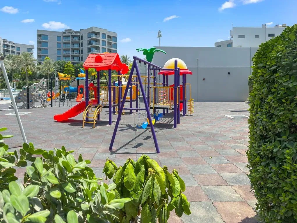 Colorful children's playground with slides and climbing frames in a paved outdoor courtyard, tall buildings in the background.