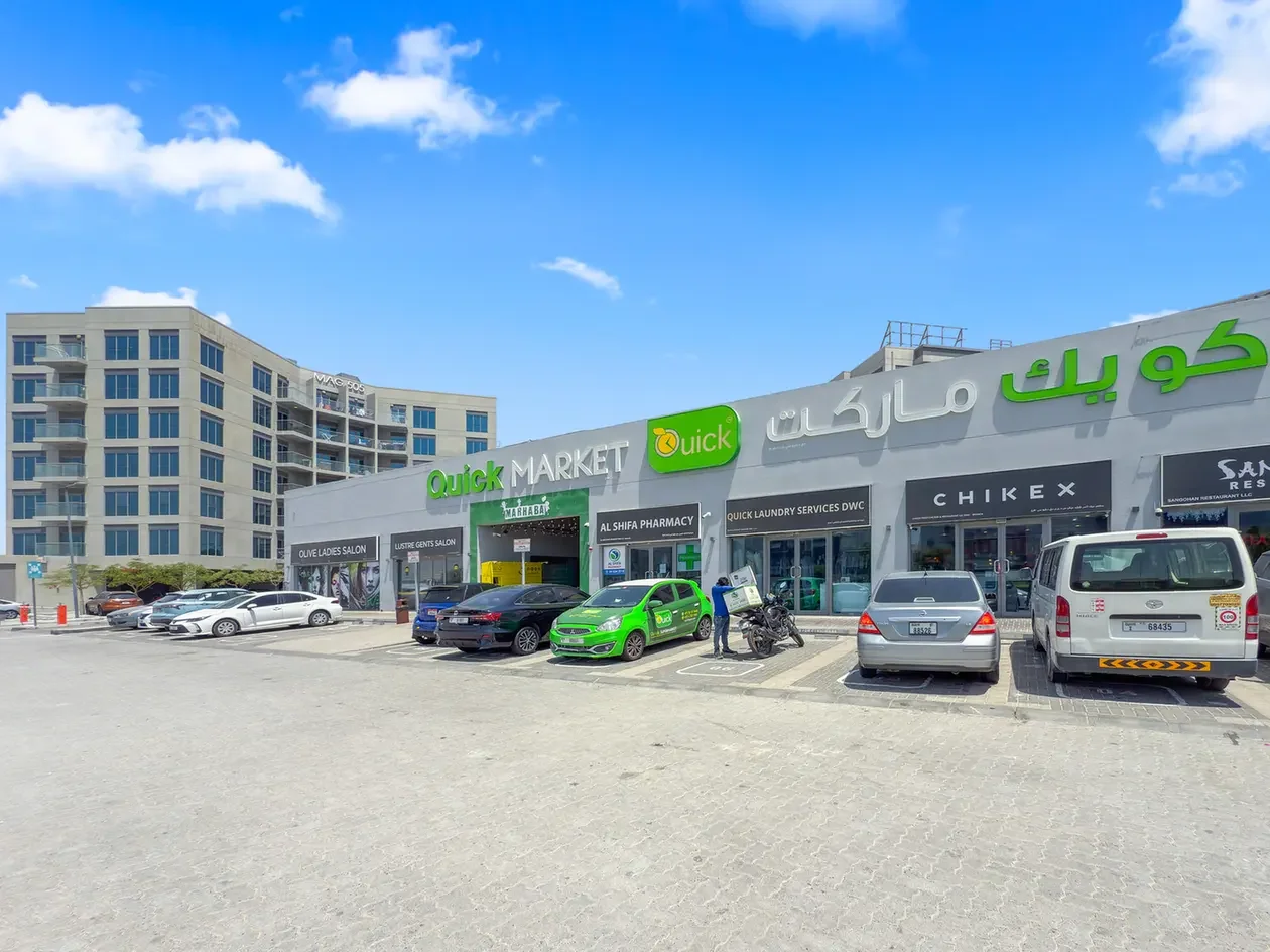 Exterior of a shopping center with a Quick Market storefront and cars parked in front under a blue sky