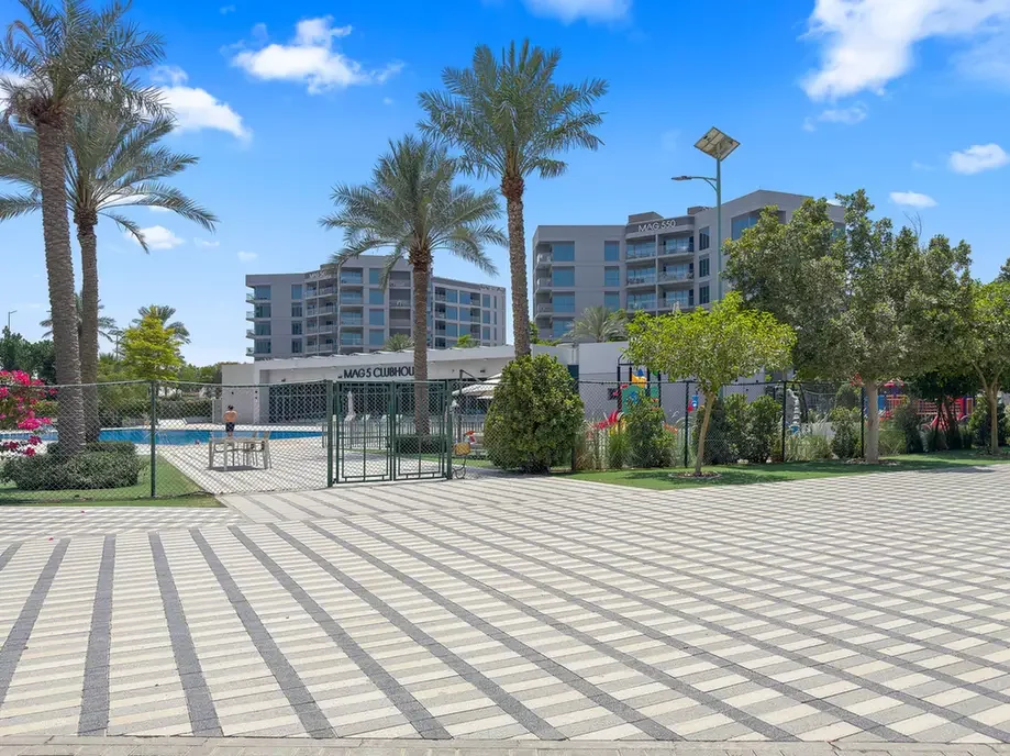 Gated clubhouse area with a swimming pool, palm trees, and modern buildings in a sunny resort courtyard.