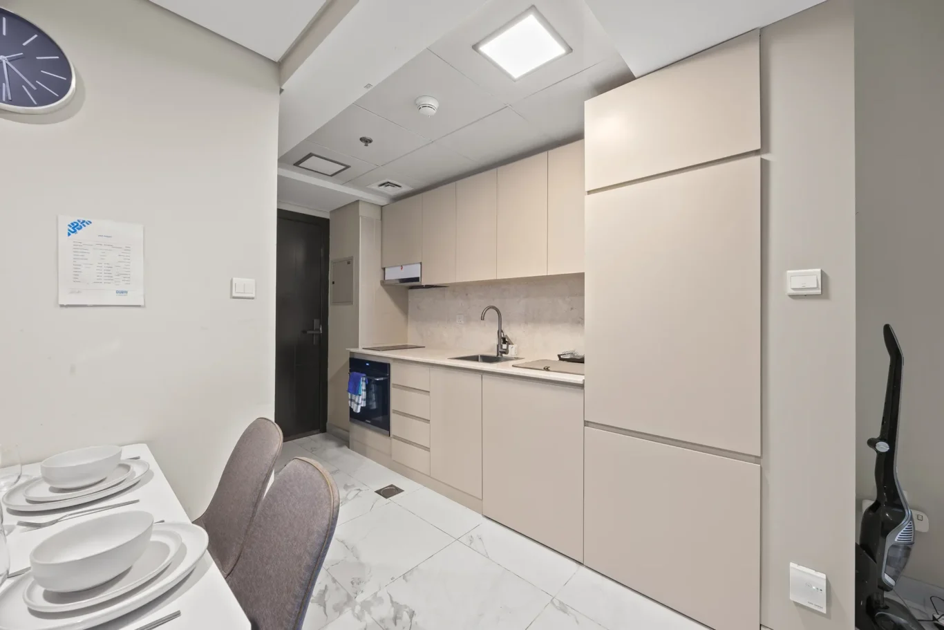 Modern kitchen with beige cabinets, marble floor, and dining table set with plates visible to the left.