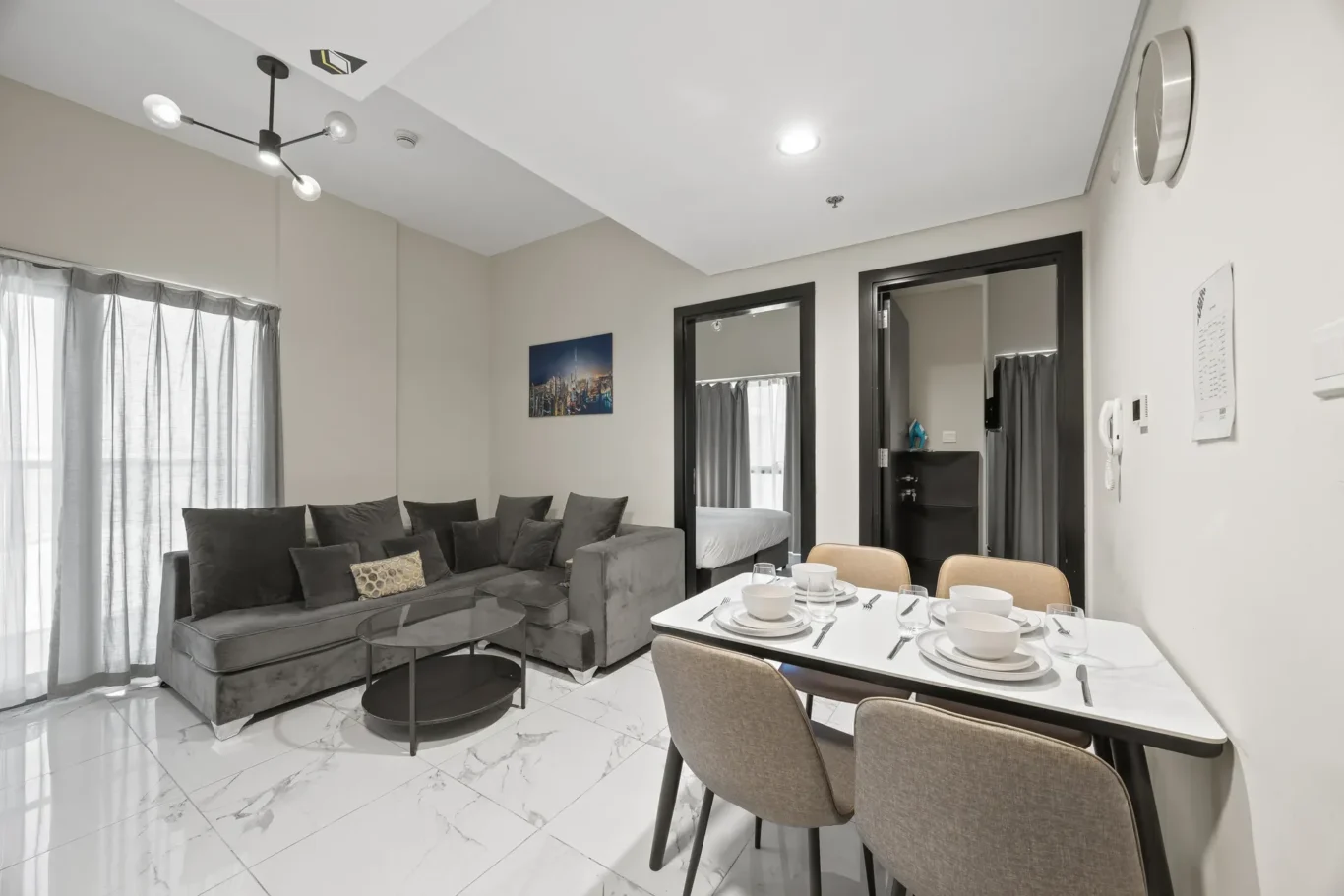 Modern open-plan living and dining space: gray sectional sofa, round glass coffee tables, and a white dining table set for six with place settings.