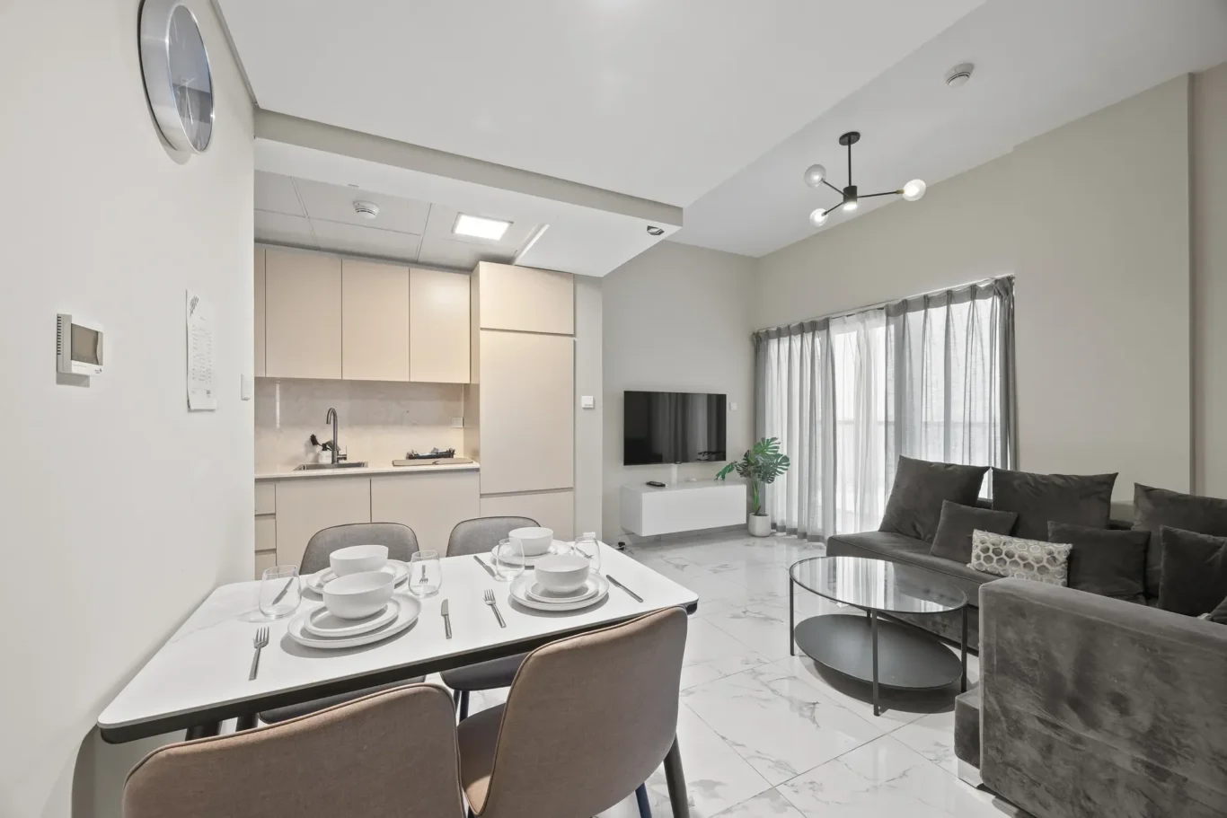 Open-plan living area with a beige kitchen, a dining table set for six, and a gray sofa area.
