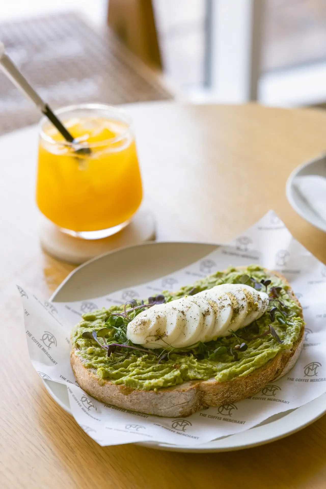 Avocado toast topped with burrata and microgreens on a toasted slice, with a glass of orange juice in the background.