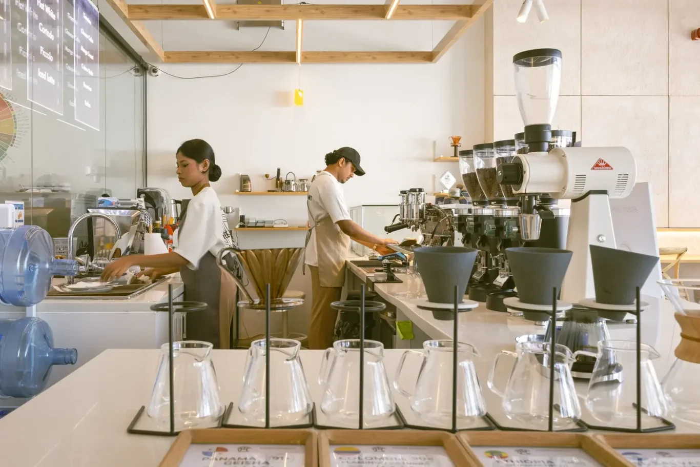 Barista station with espresso machine and grinders, two workers preparing drinks behind a counter