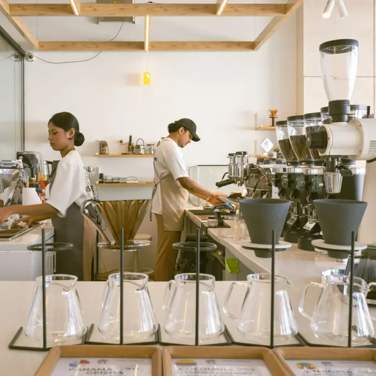 Barista station with espresso machine and grinders, two workers preparing drinks behind a counter