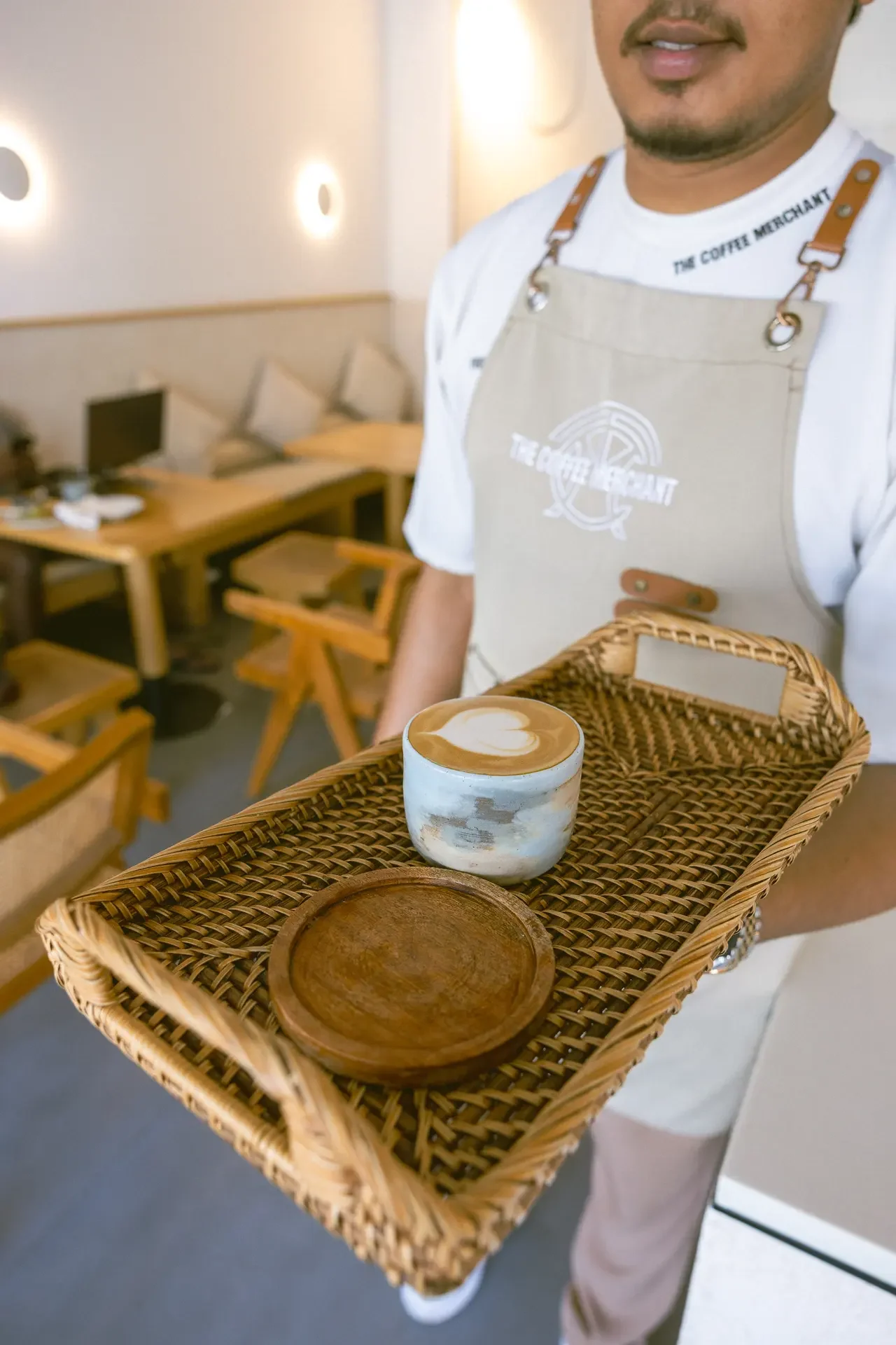 Barista in an apron presenting a wicker tray with a blue cup of latte art in the foreground.