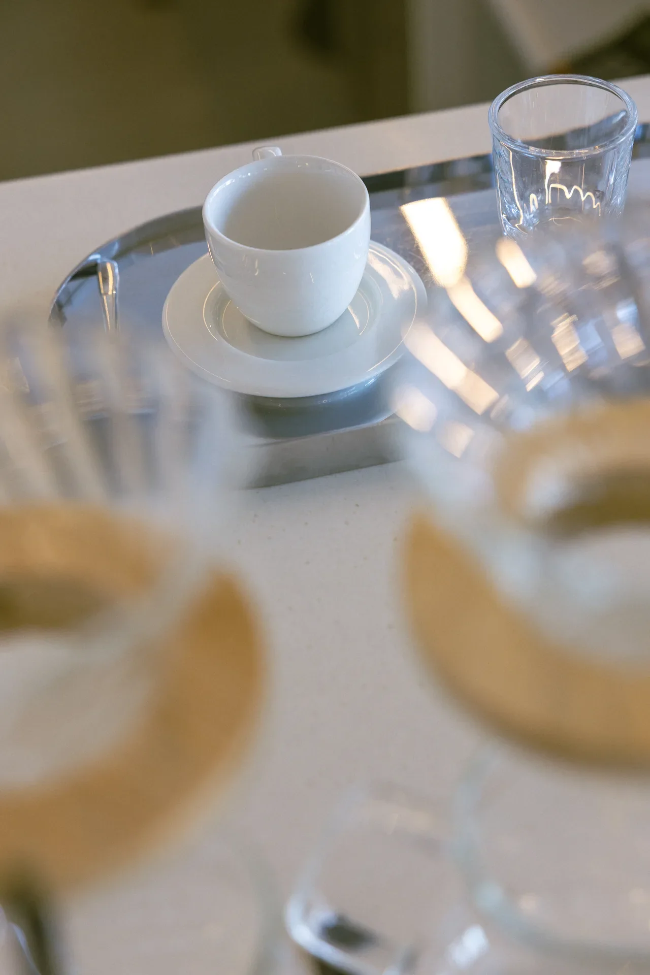 White ceramic cup on a saucer with an empty interior, set on a reflective glass table beside a clear glass.