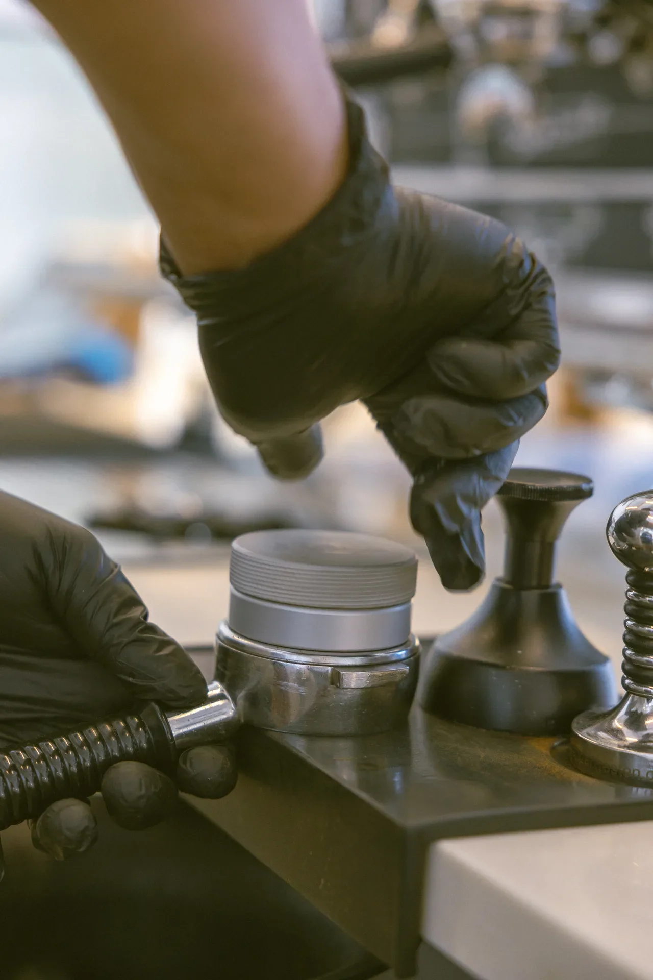 Close-up of gloved hands attaching a metal hose connector to a valve on a workshop bench, with tools nearby