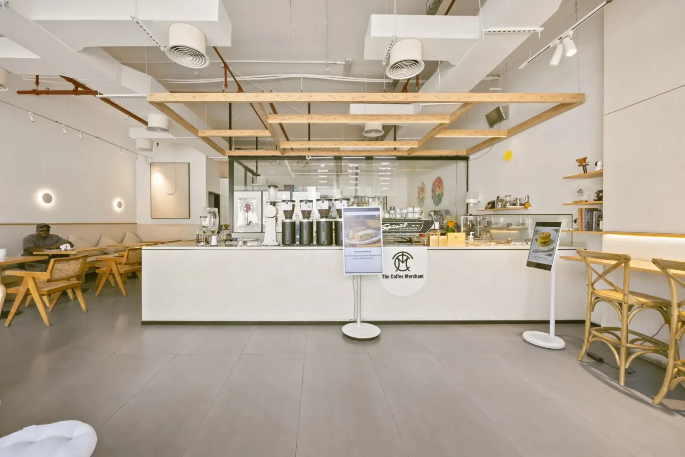 Bright, modern coffee shop interior with a white counter, espresso machines, and exposed wooden beams overhead.