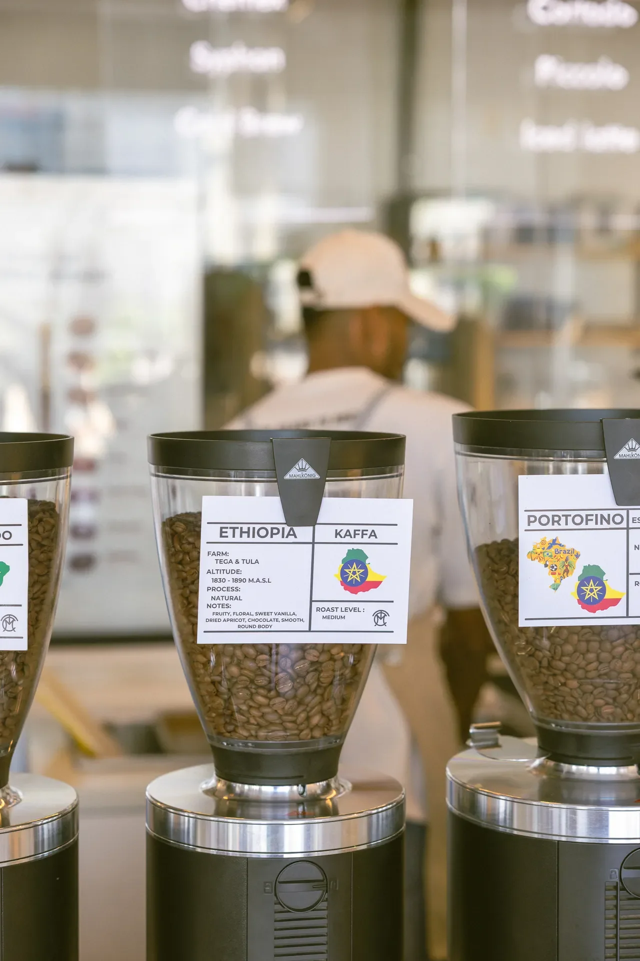 Row of coffee grinders with glass jars labeled Ethiopia and Kaffa on a shop counter.