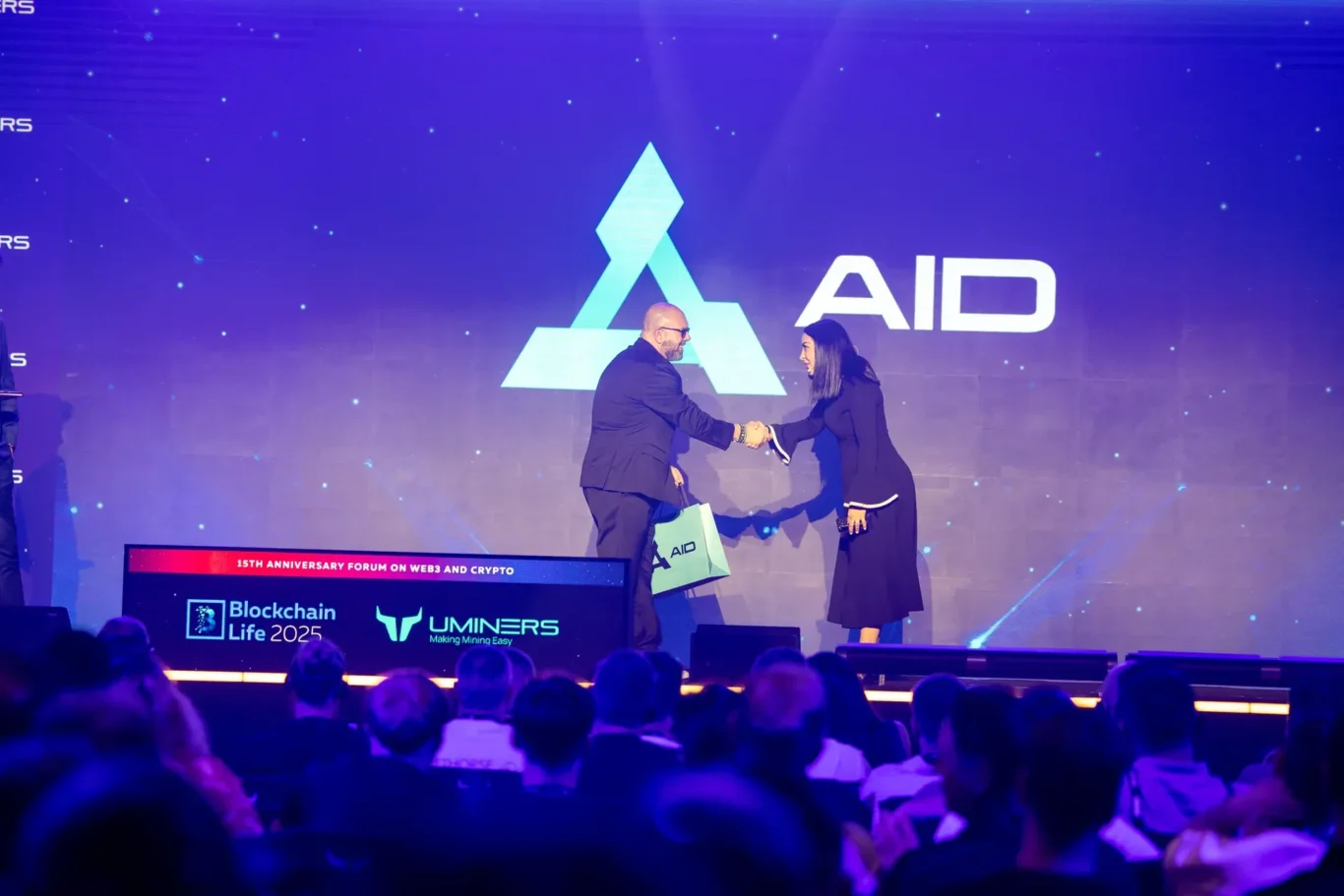 AID on the Blockchain Life main stage under its own branding. Event photography by MRPS at Blockchain Life 2025, Festival Arena, Dubai.