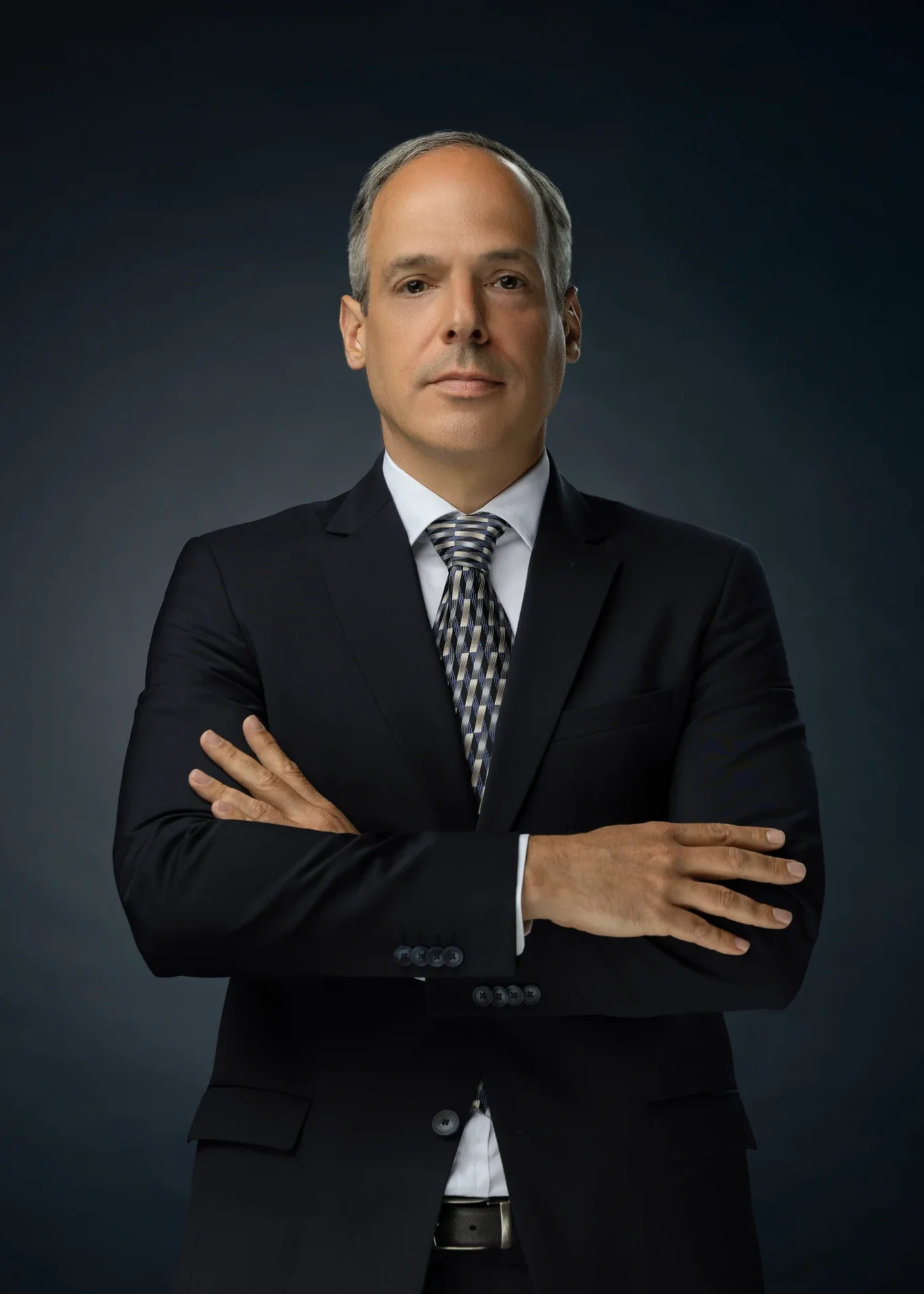 Executive in a navy suit with arms crossed against a dark blue backdrop. Corporate business portrait of a Dubai CEO, photographed at the MRPS studio in Business Bay.