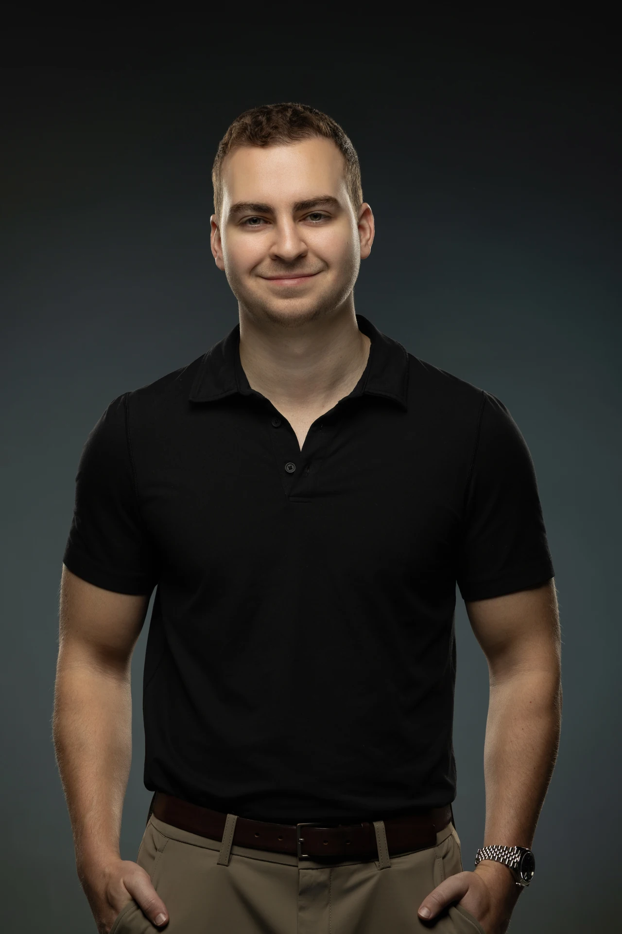 Smiling portrait in a black polo shirt on a dark grey backdrop. Professional headshot of Tim Ruscica of Tech With Tim, photographed at the MRPS studio in Dubai.