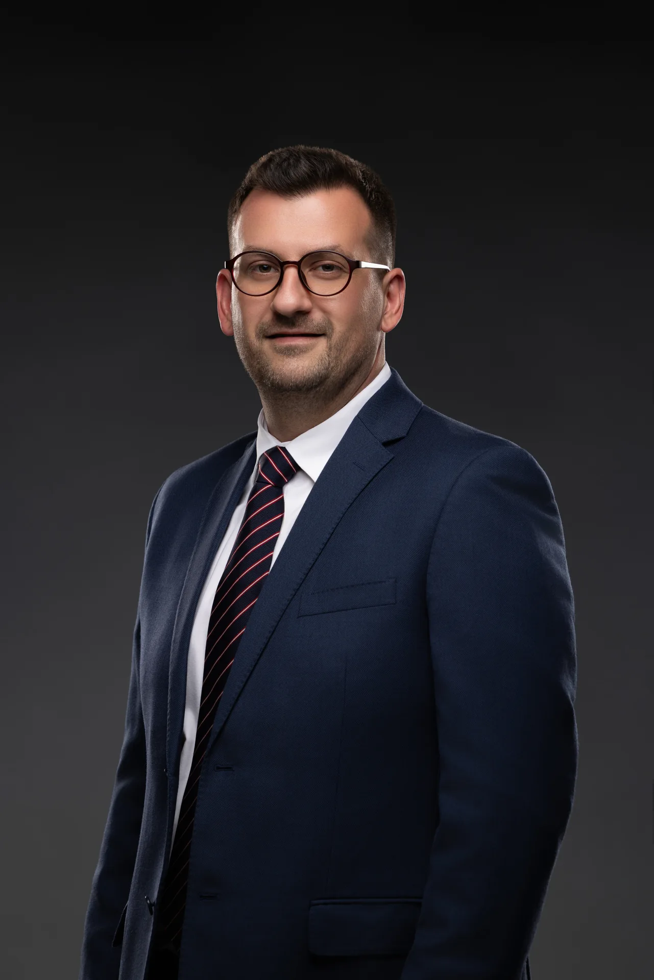 CEO headshot in a navy suit and striped tie on a dark backdrop. Photographed at the MRPS studio in Business Bay, Dubai.
