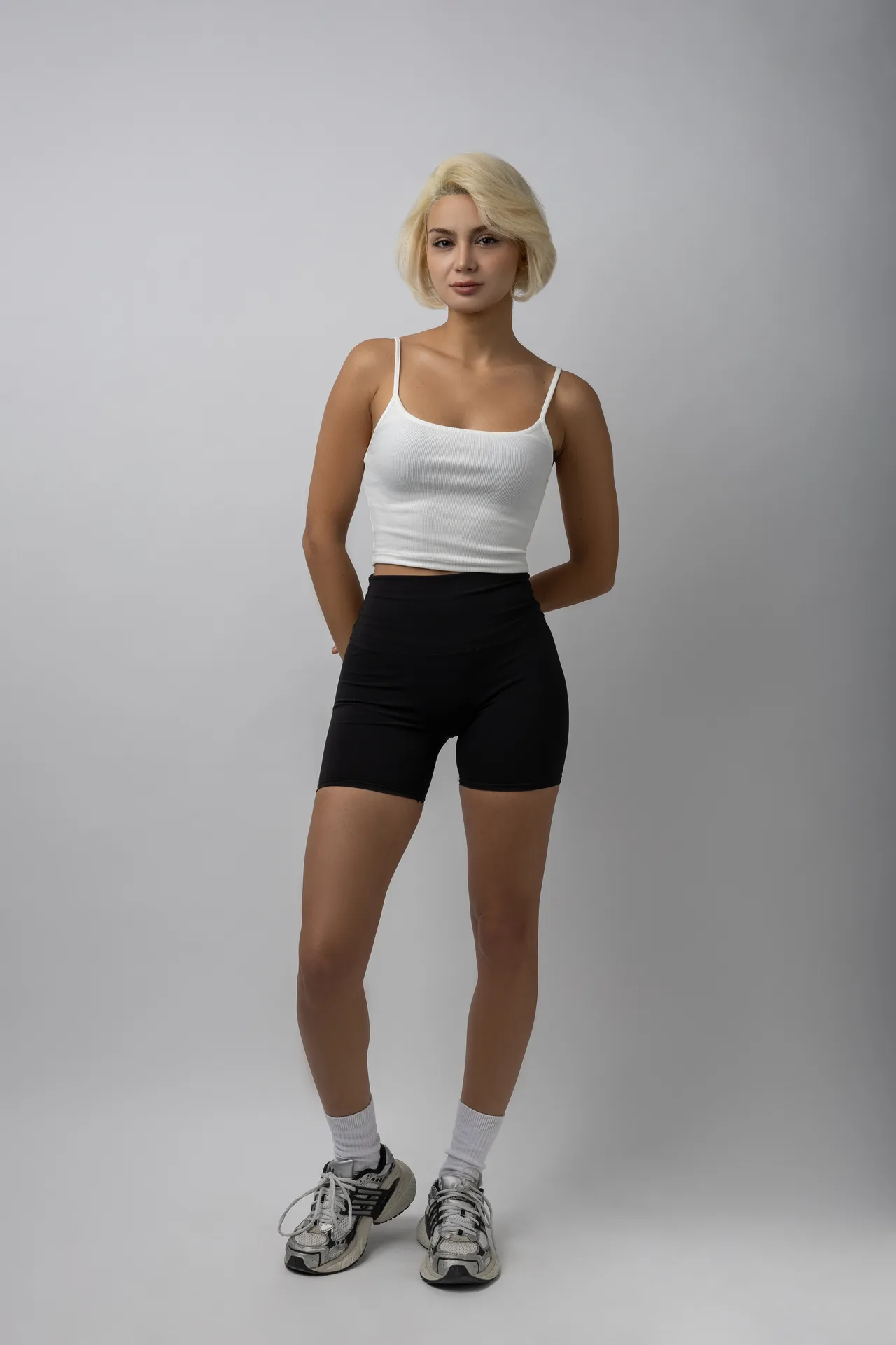 Full-length front digital of model Dr. Aysan Soleymani in a white tank top and black shorts on a light grey backdrop.