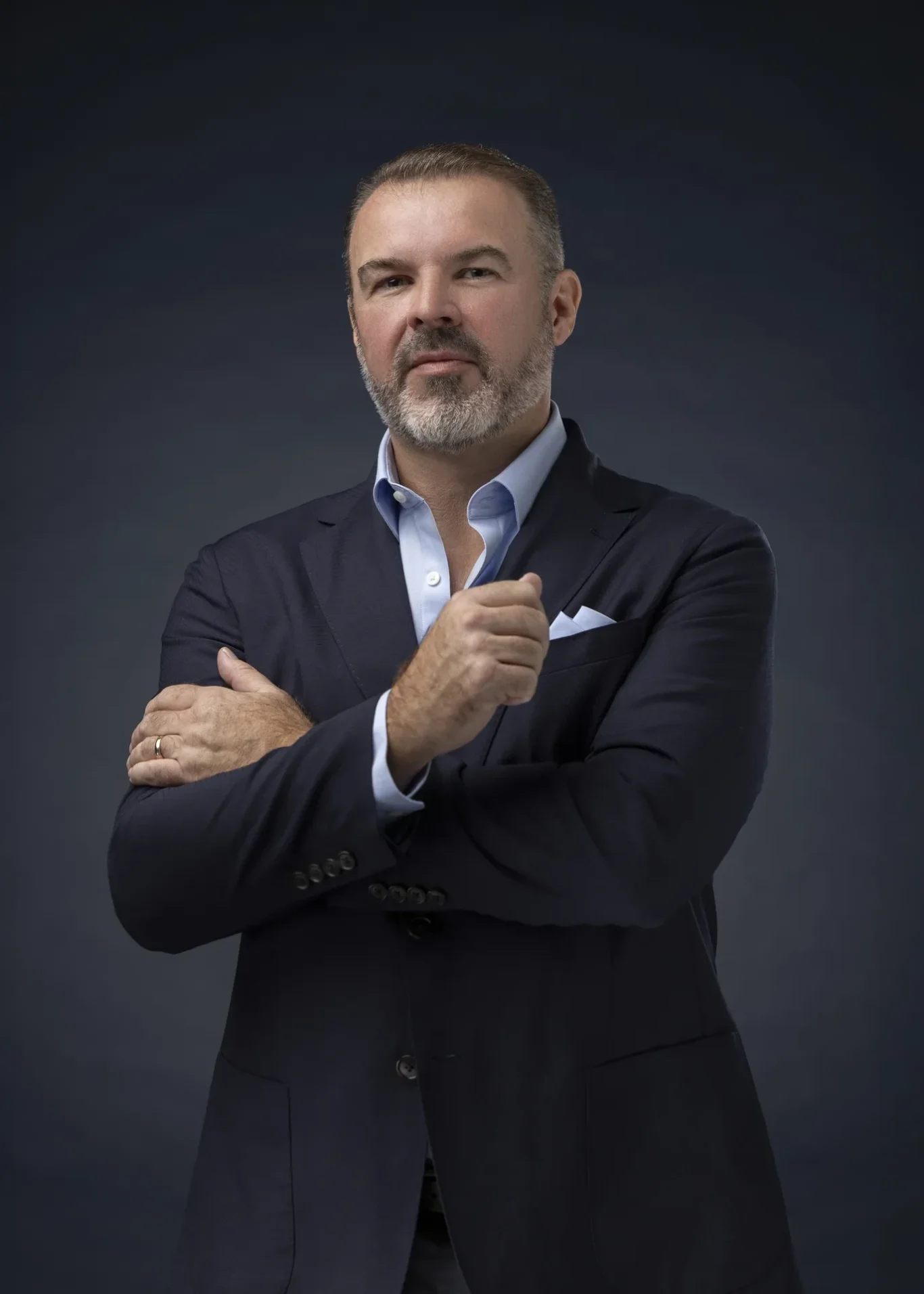 Rik Williams in a navy blazer and light blue shirt with arms crossed on a dark navy backdrop. Corporate portrait photography by MRPS in Dubai, photographed by Nastaran.