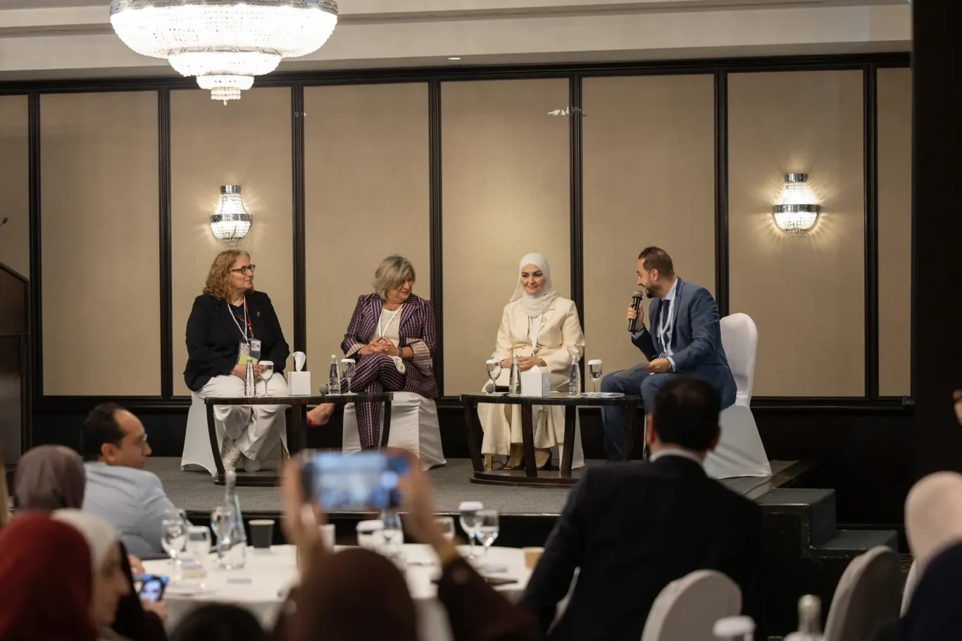 Four panellists in conversation on stage under the ballroom chandeliers while the audience listens. Corporate event photography by MRPS for My Arabic Publishing at Movenpick Grand Al Bustan, Dubai.