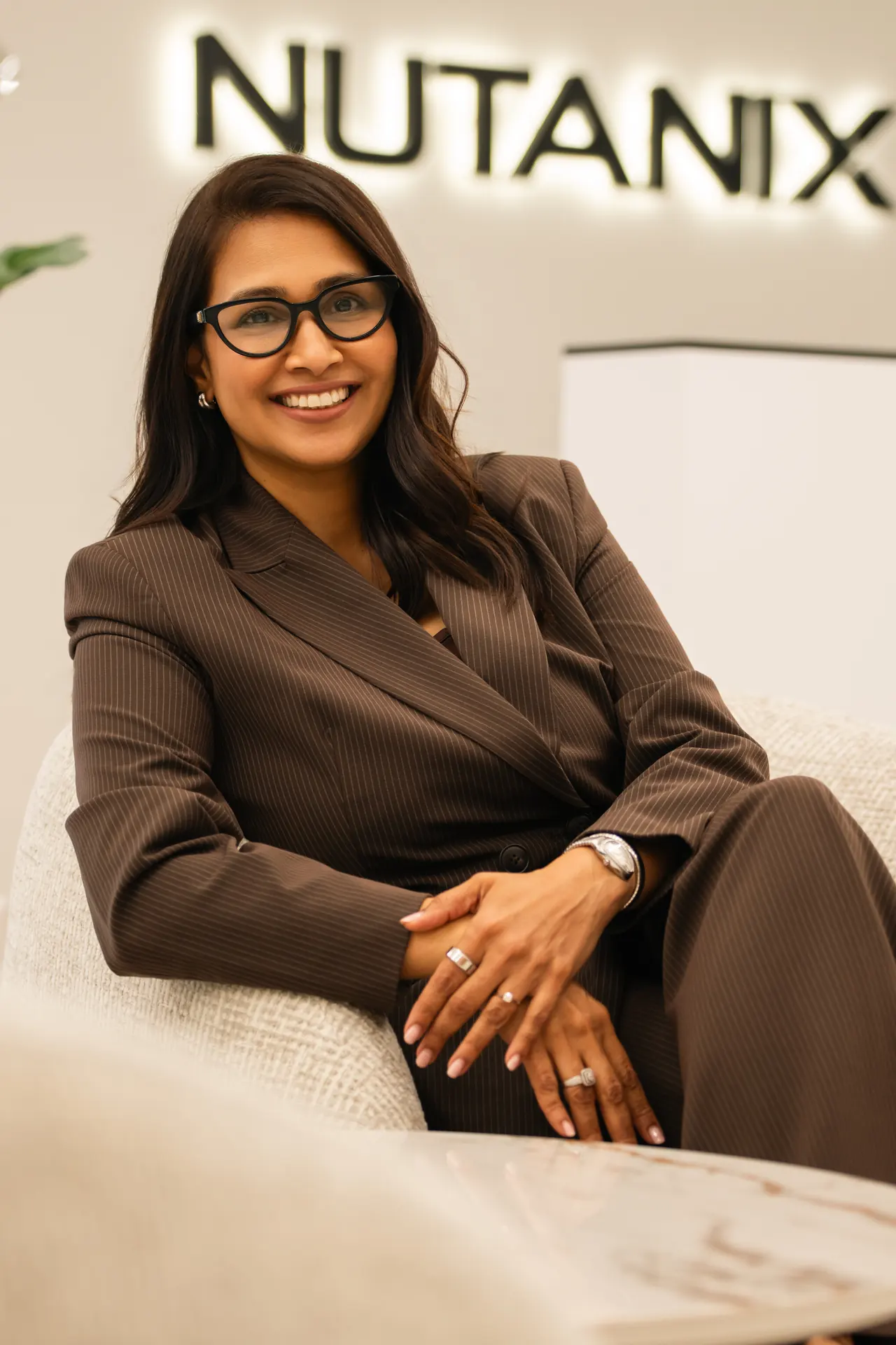 Seated executive in a brown suit beside the Nutanix logo wall. On-site corporate headshot at the Nutanix office in Dubai.