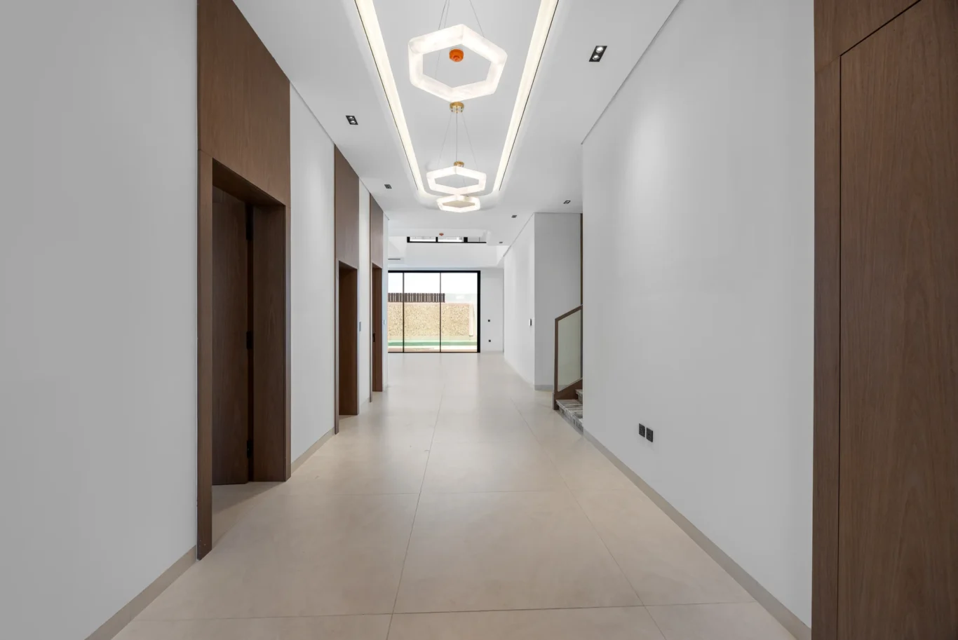 Entrance hallway with hexagonal ceiling lights and walnut doors, unfurnished five-bedroom villa in Al Furjan, Dubai.