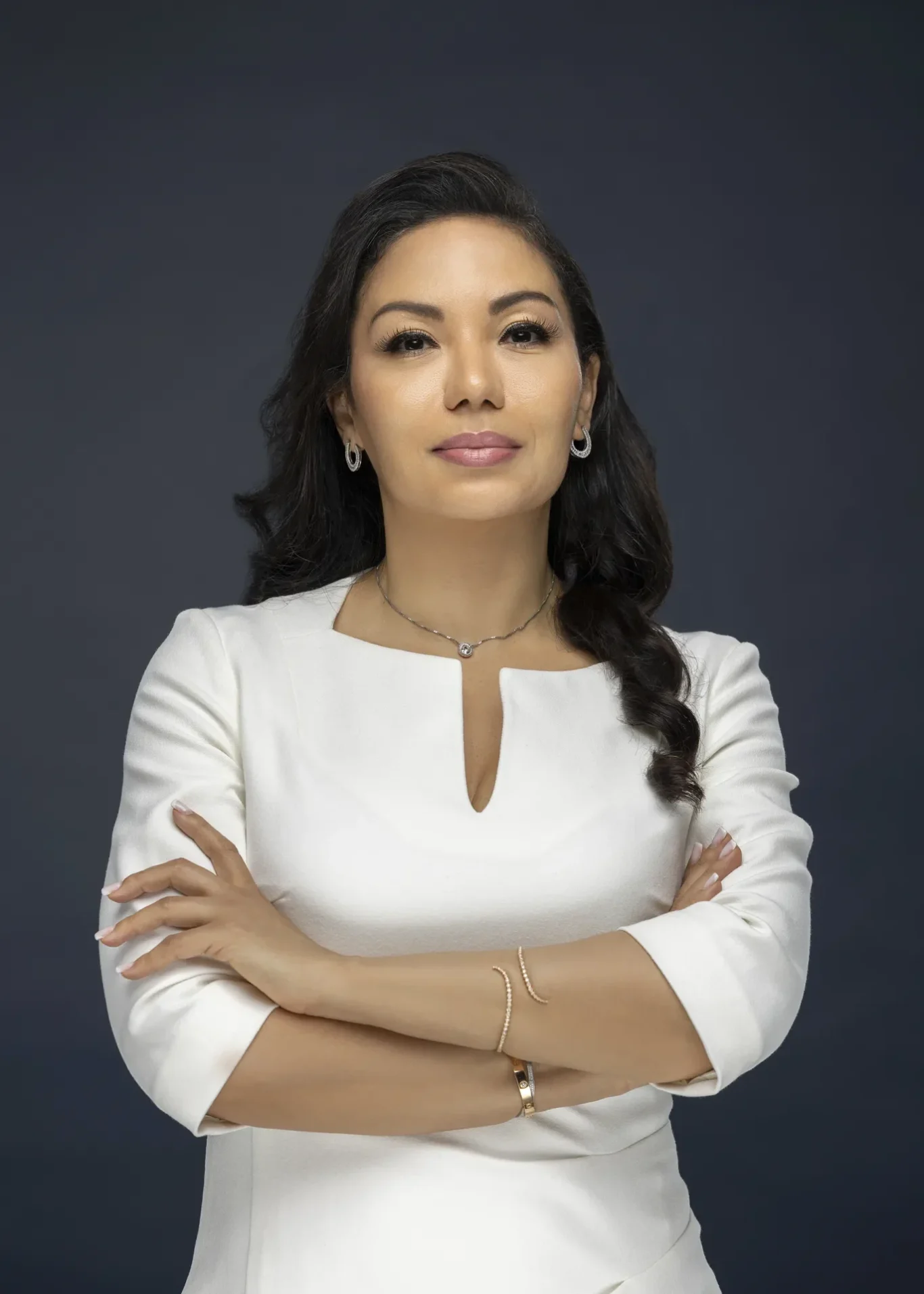 Sandra in a white dress with arms crossed on a navy backdrop, business profile portrait. Business profile and LinkedIn portrait photography by MRPS in Dubai.