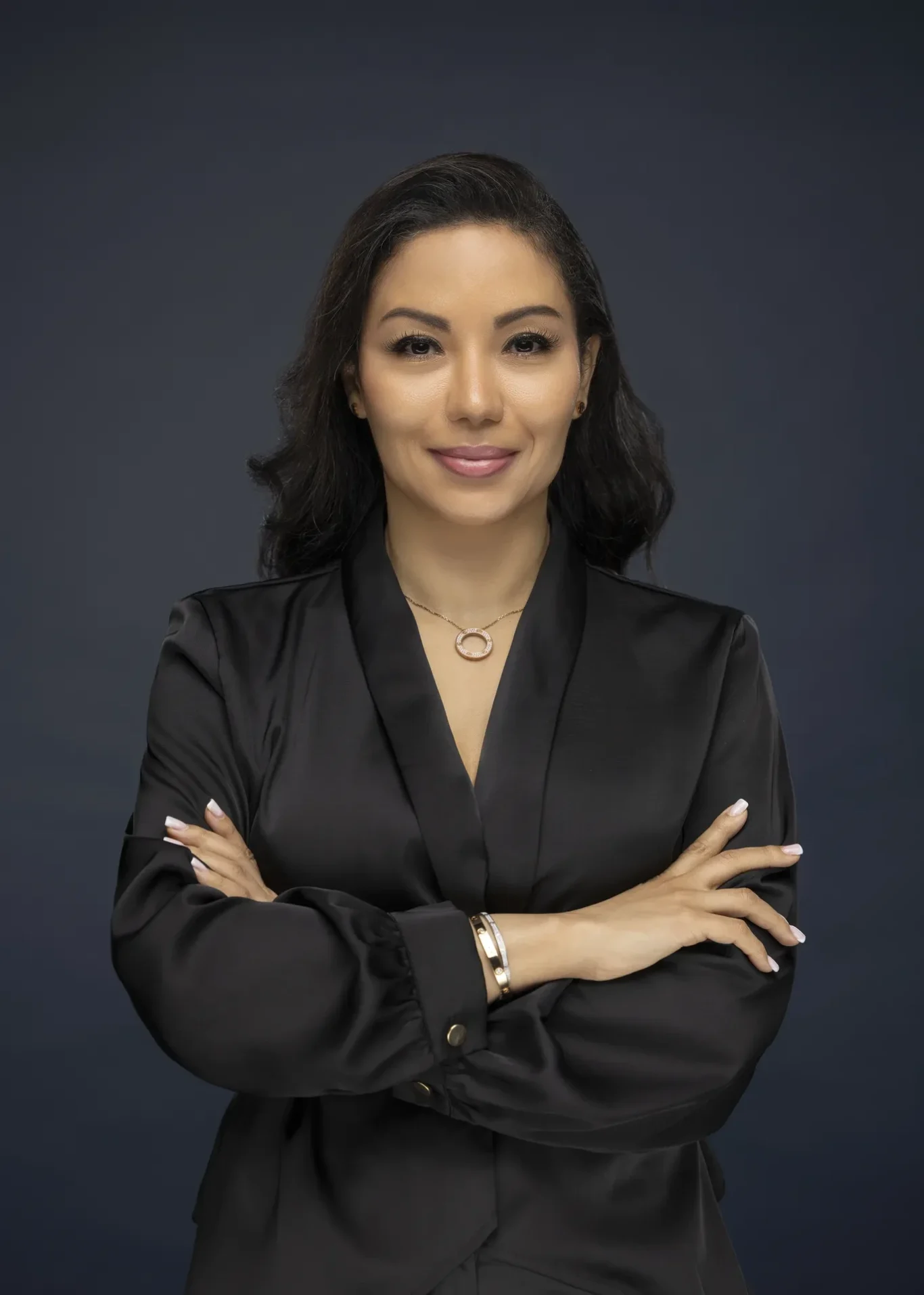 Sandra in a black satin shirt with arms crossed on a dark navy backdrop. Business profile and LinkedIn portrait photography by MRPS in Dubai.