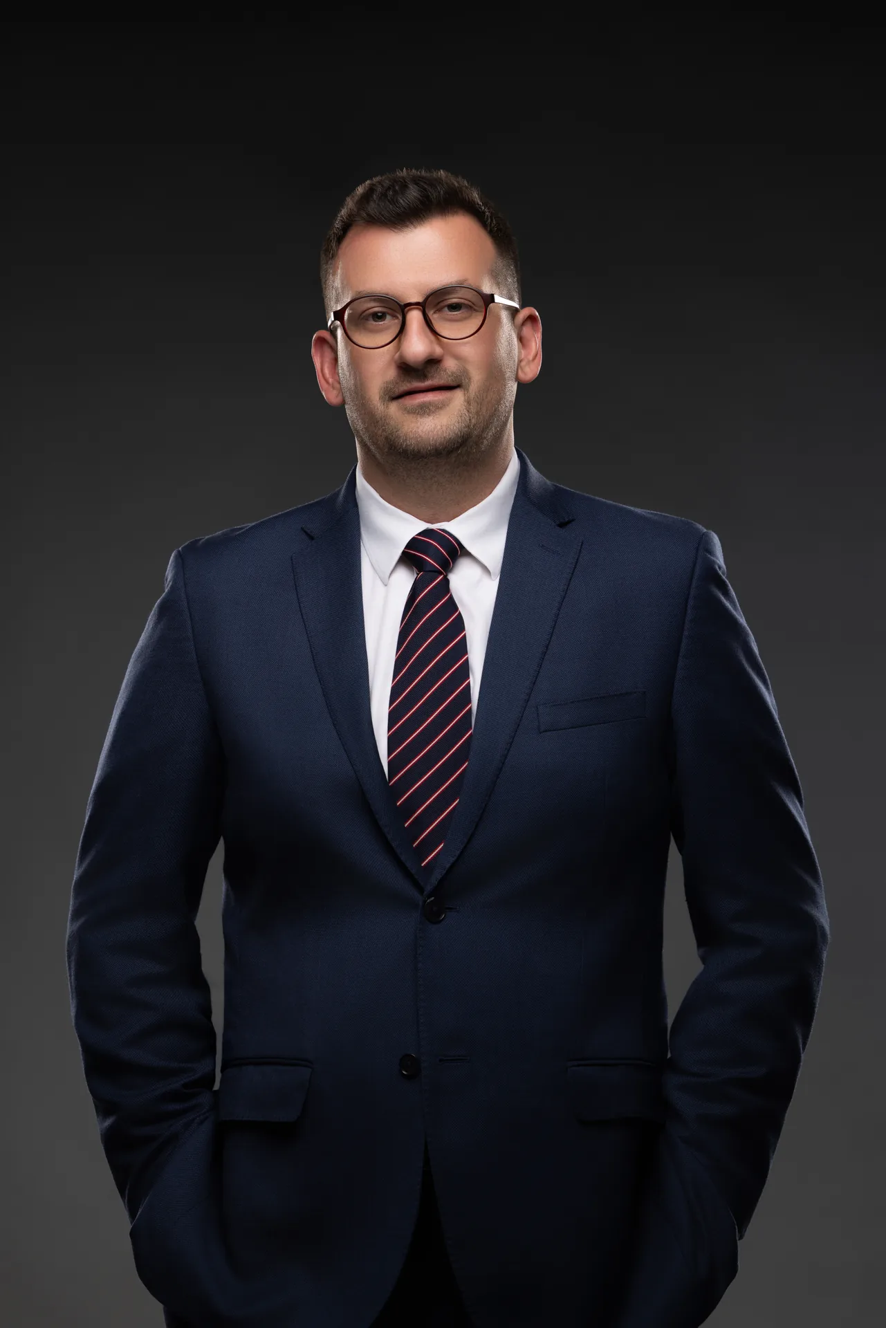 Standing CEO portrait with hand in pocket, navy suit and glasses. Photographed at the MRPS studio in Business Bay, Dubai.