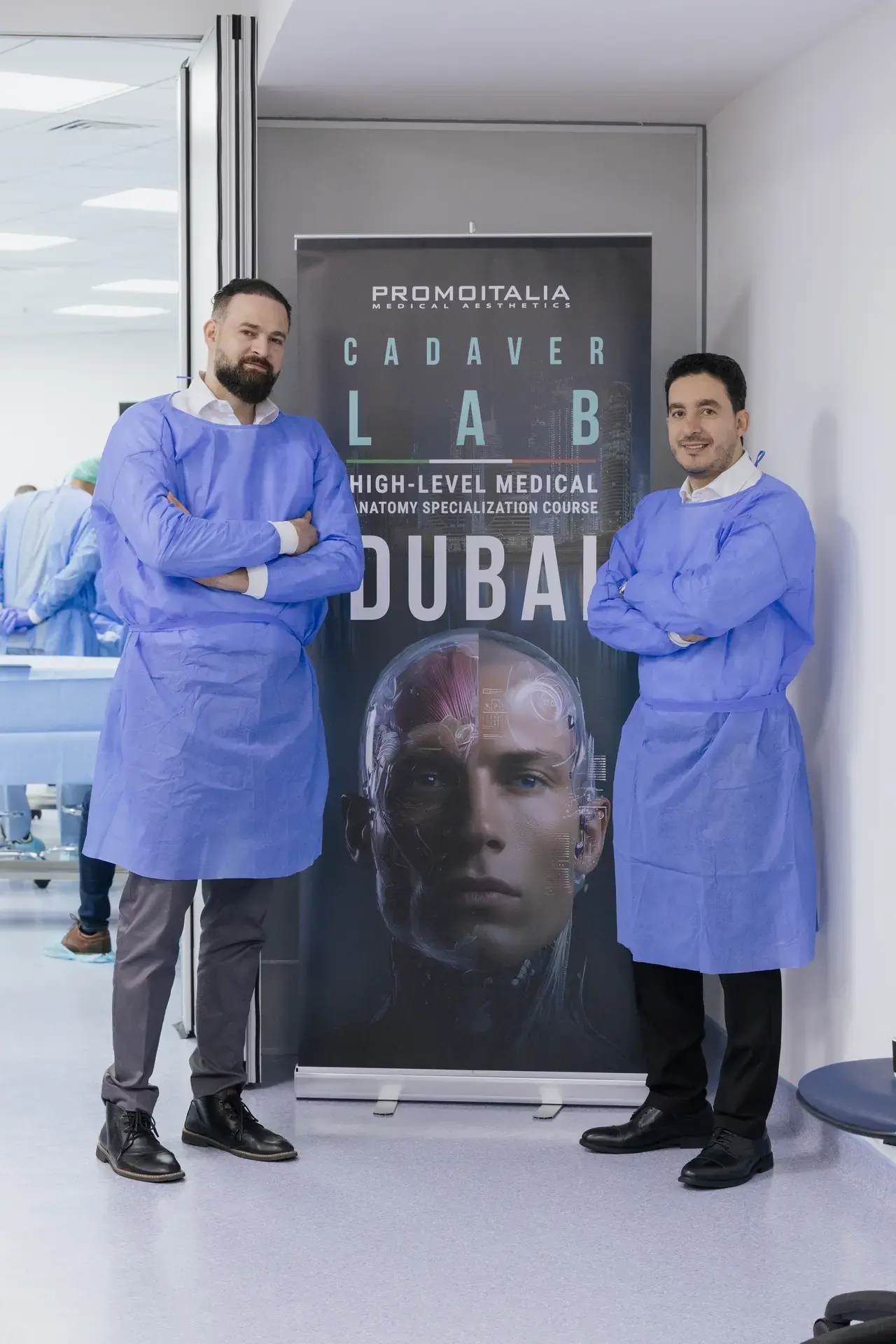 Two faculty members in surgical gowns beside the Cadaver Lab Dubai course banner. Event photography by MRPS at the Promoitalia Cadaver Lab medical anatomy course in Dubai.