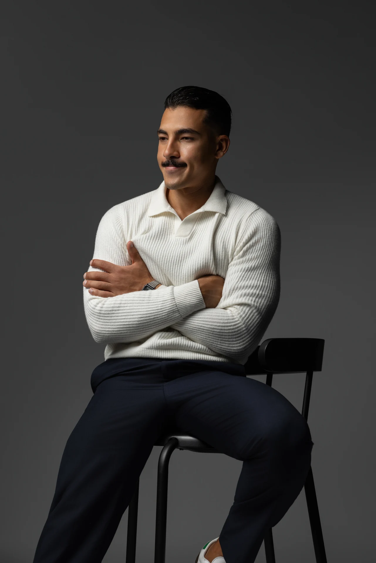 Seated portrait in a cream knit polo with arms crossed, looking off camera. Male modeling portfolio photoshoot by MRPS in Dubai, photographed by Nastaran.
