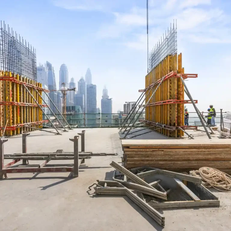 Construction site on a rooftop with wooden and metal formwork, rebar, and workers; city skyline in the distance. Construction progress photography by MRPS at the Emaar tower in Dubai Marina.