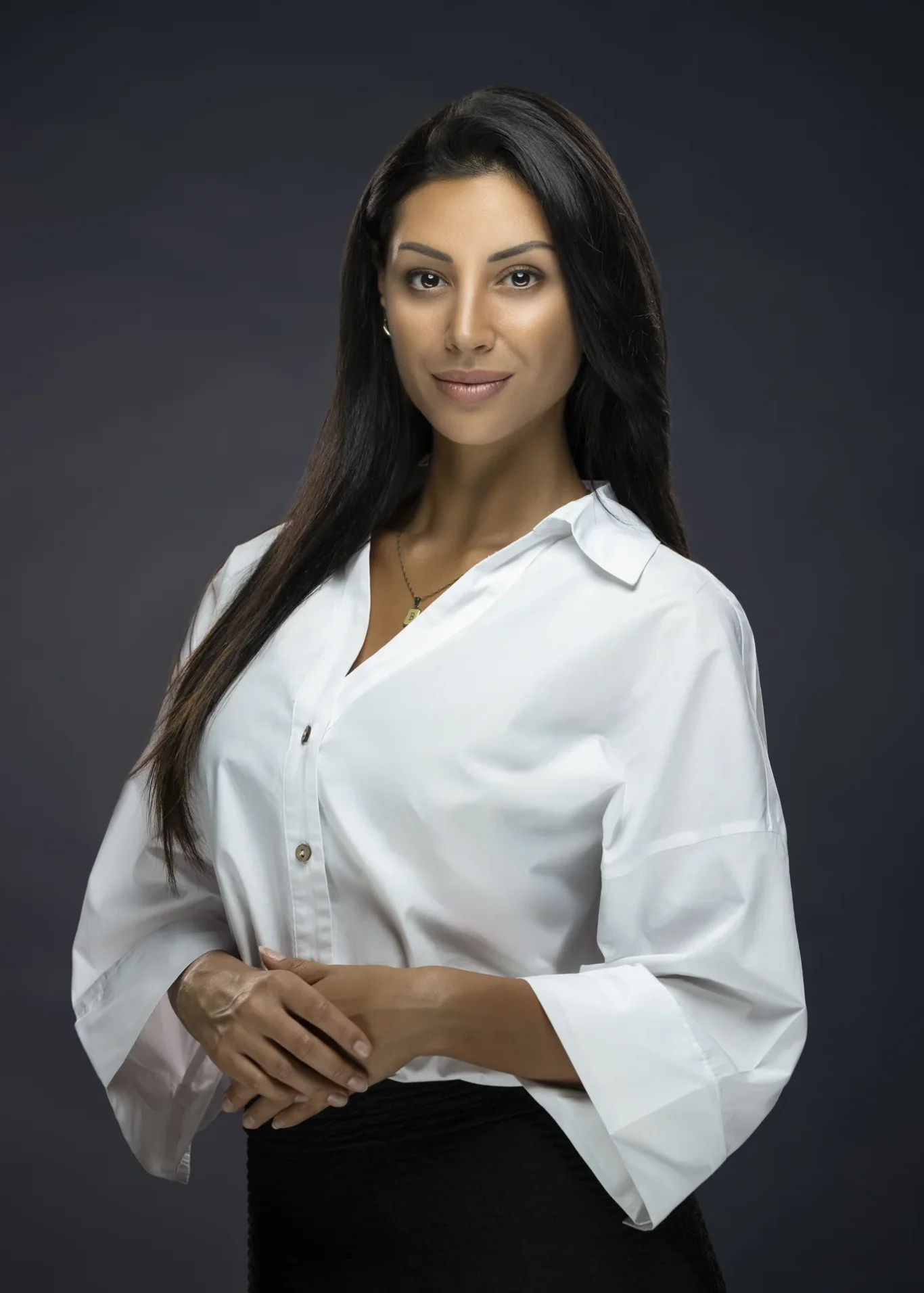 Real estate broker portrait of Berna with hands together on a dark grey backdrop, for LinkedIn and her business website.