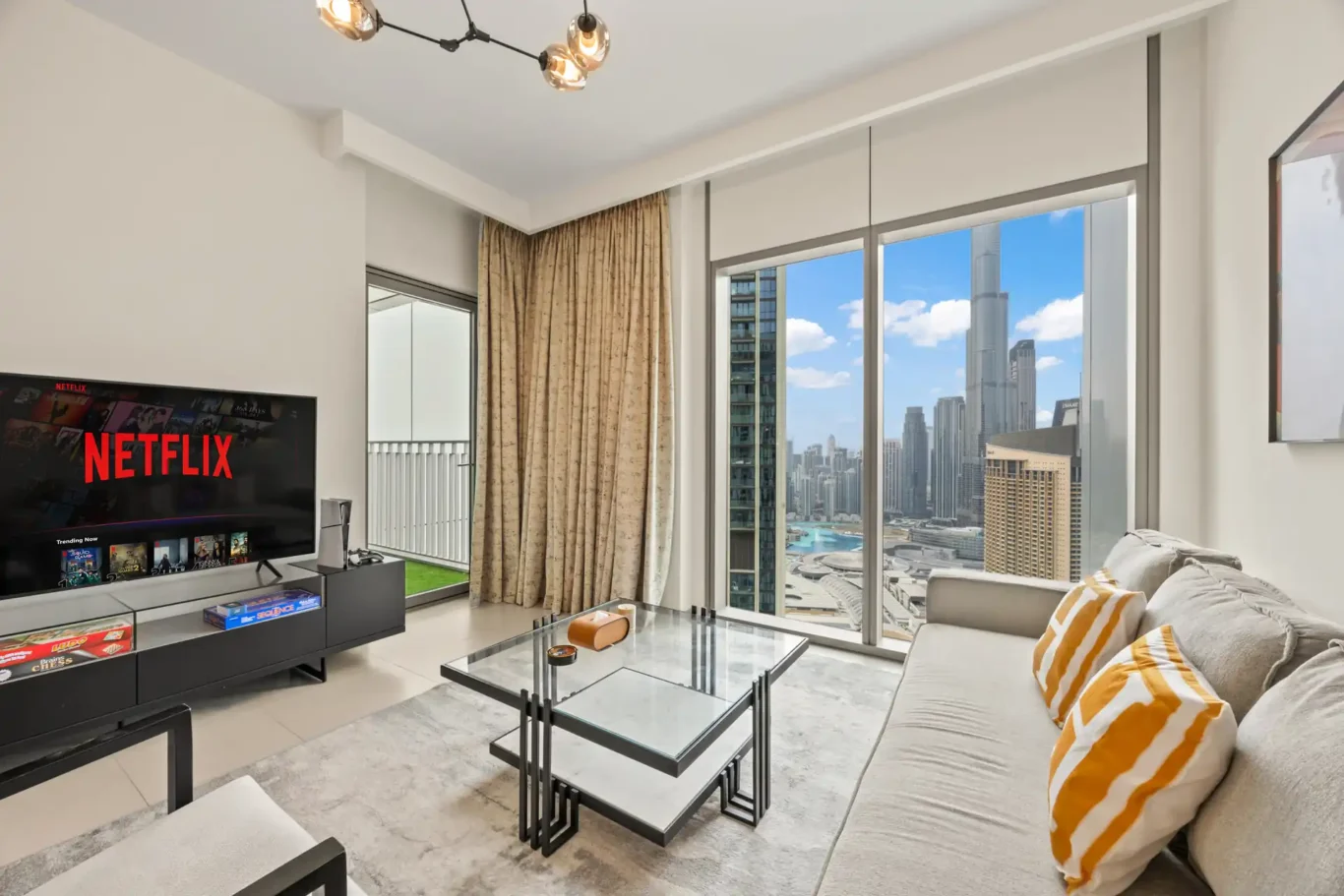 Living room with wall mounted TV, orange cushions and the balcony door. Day, twilight and night Airbnb photography by MRPS for Vista Haus Holiday Homes in Downtown Dubai.